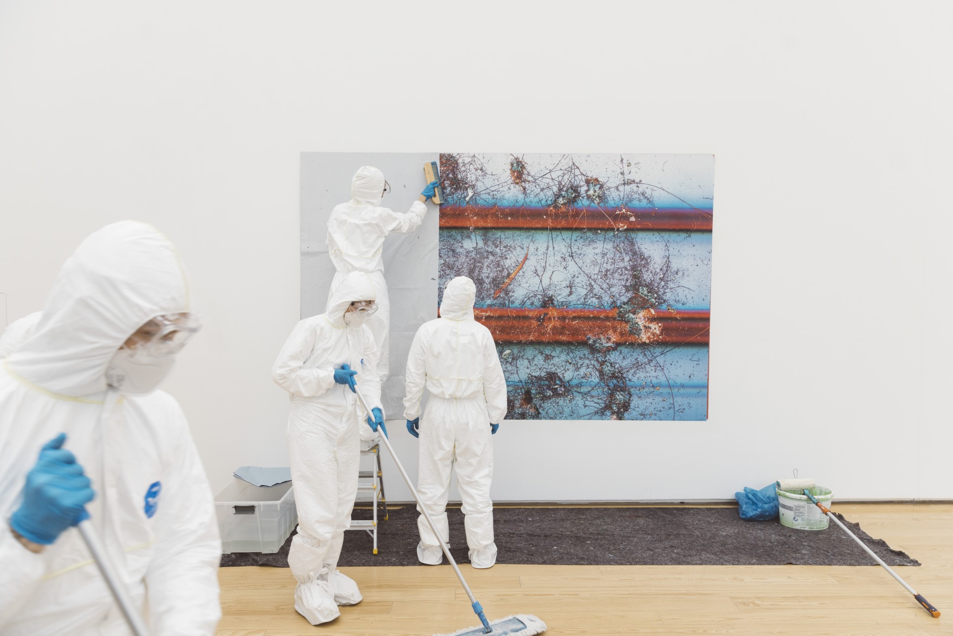 Einige Personen in Schutzanzügen reinigen den Boden vor einer großen Wandinstallation.