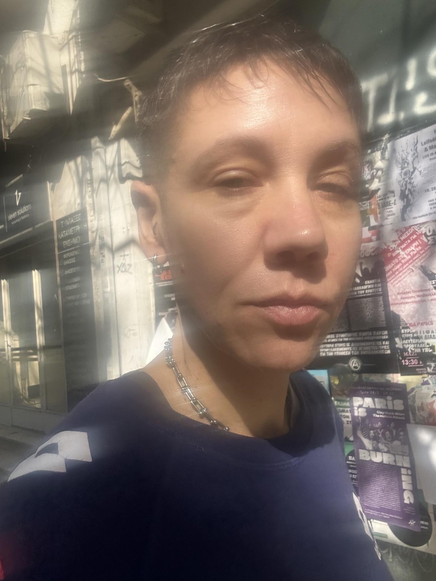 Nahaufnahme einer Person mit kurzem Haar, die in die Kamera blickt, vor einem Hintergrund mit Plakaten.