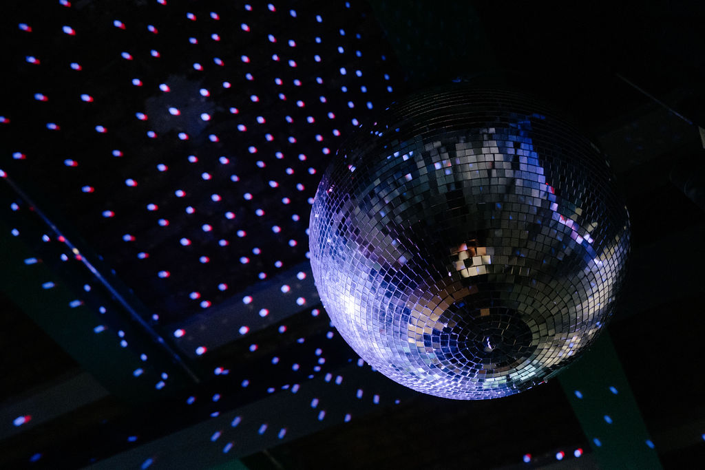 Glitzernde Discokugel wirft buntes Licht auf einen dunklen Hintergrund.