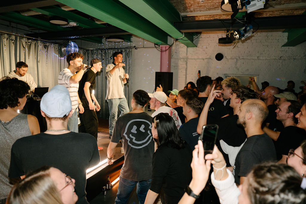 Zwei Musiker treten live vor einer begeisterten Menge in einem Veranstaltungsraum auf.