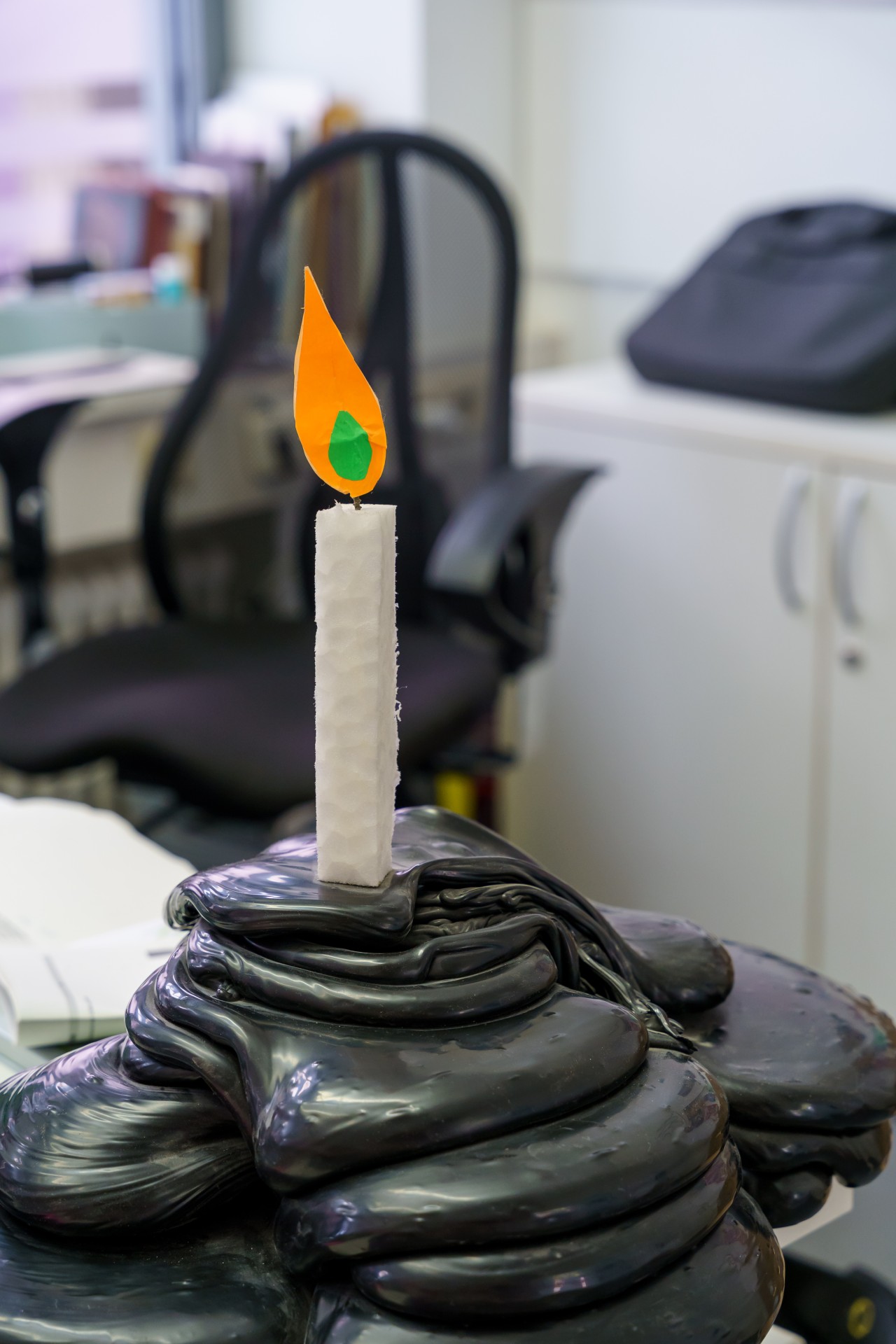 Kunstvolle Kerze auf schwarzem, geschwungenem Untergrund im Büro, mit orangefarbenem Flammendesign.