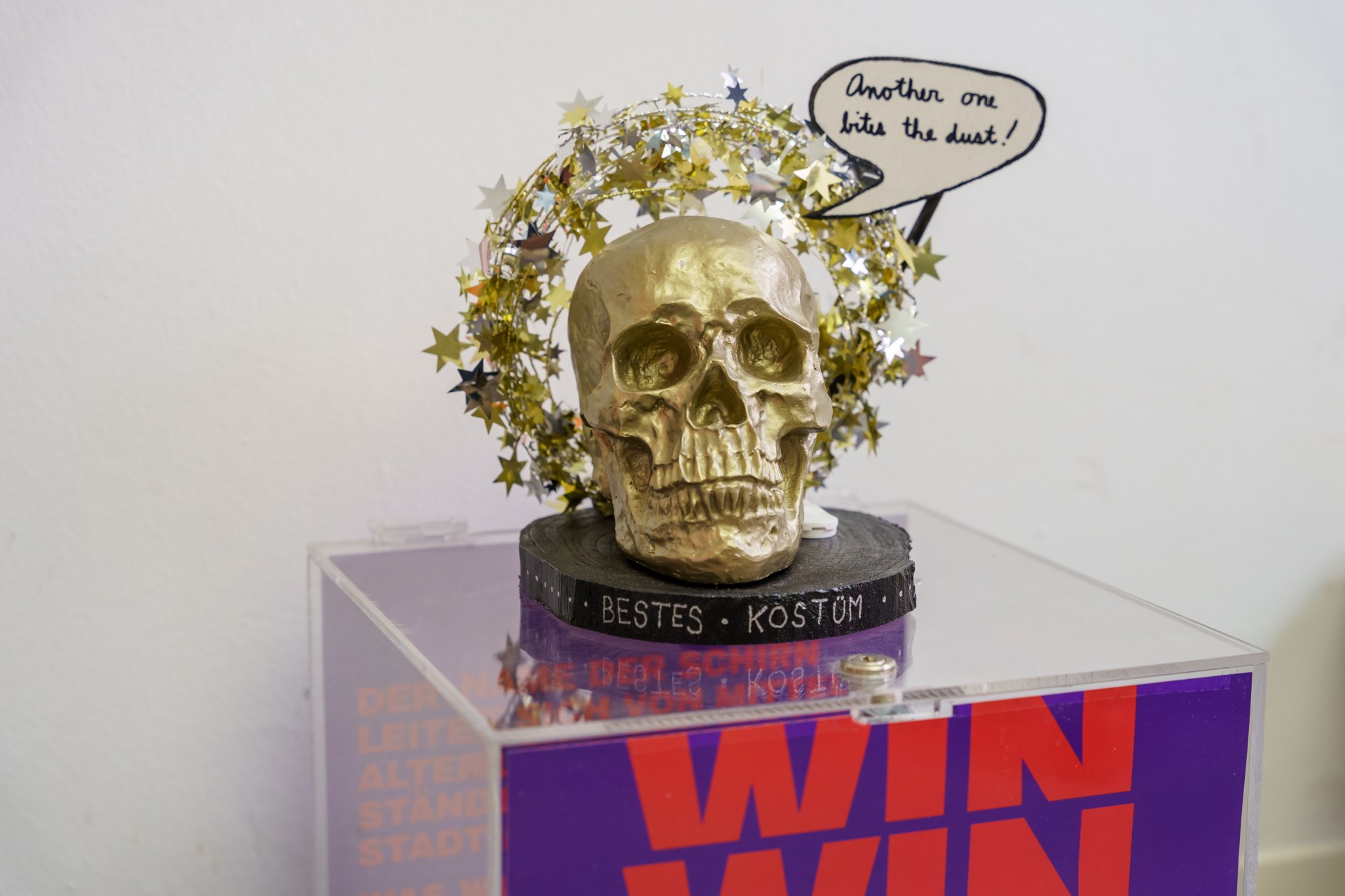 Goldener Totenkopf mit Sternenkranz und Sprechblase: „Another one bites the dust!“