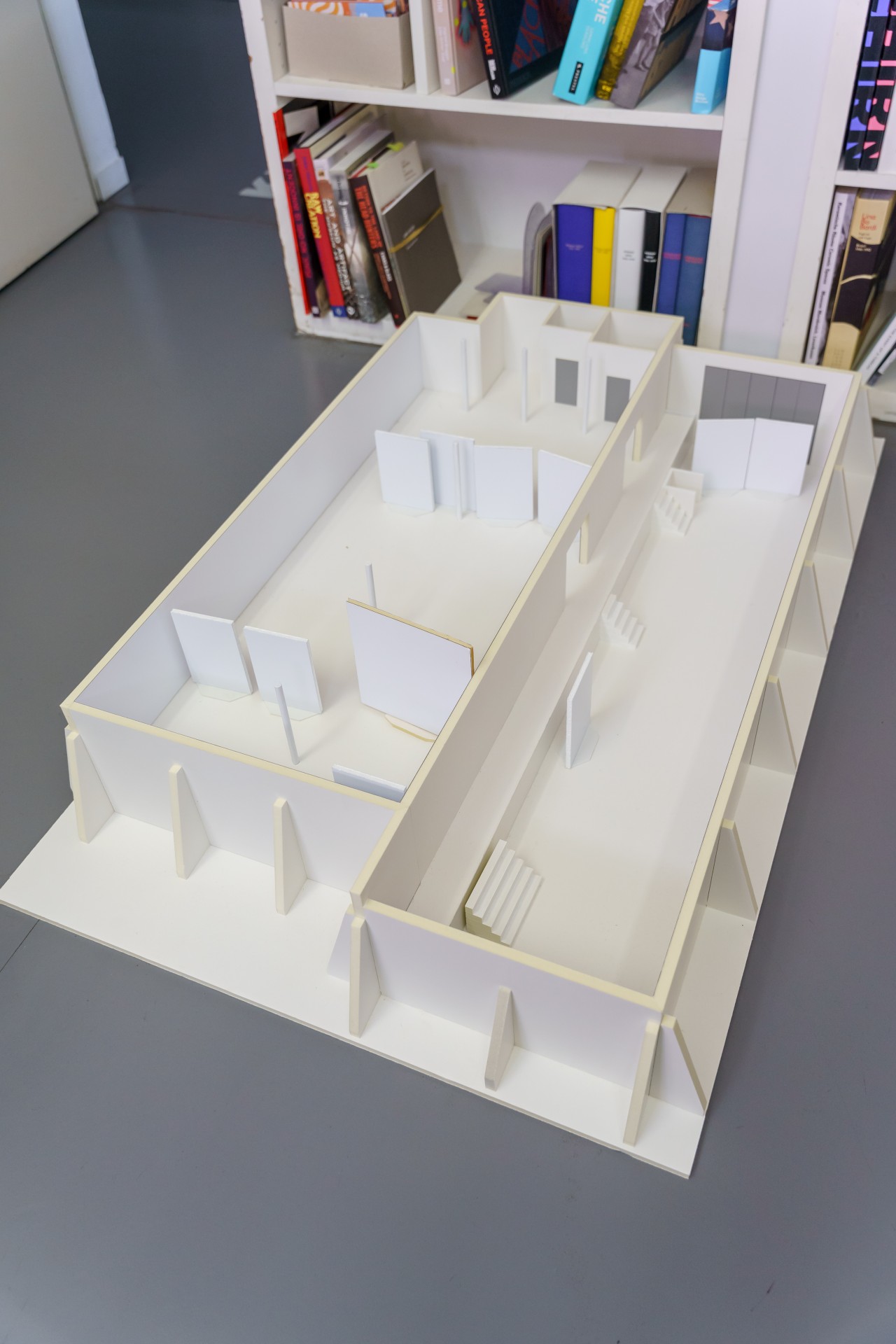 Modell eines Innenraums mit Wänden und Treppen, auf einem Tisch neben einem Bücherregal platziert.