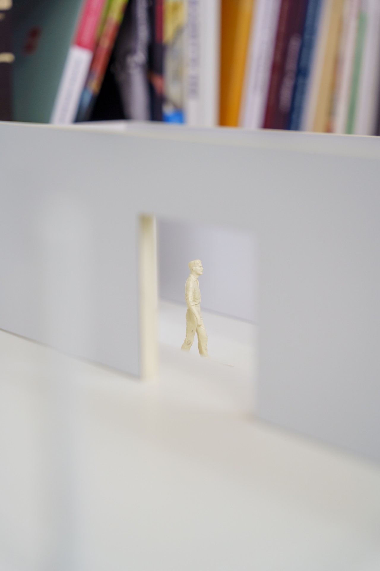 Eine kleine Figur geht durch einen offenen Durchgang in einer weißen Wand, umgeben von Bücherregalen.
