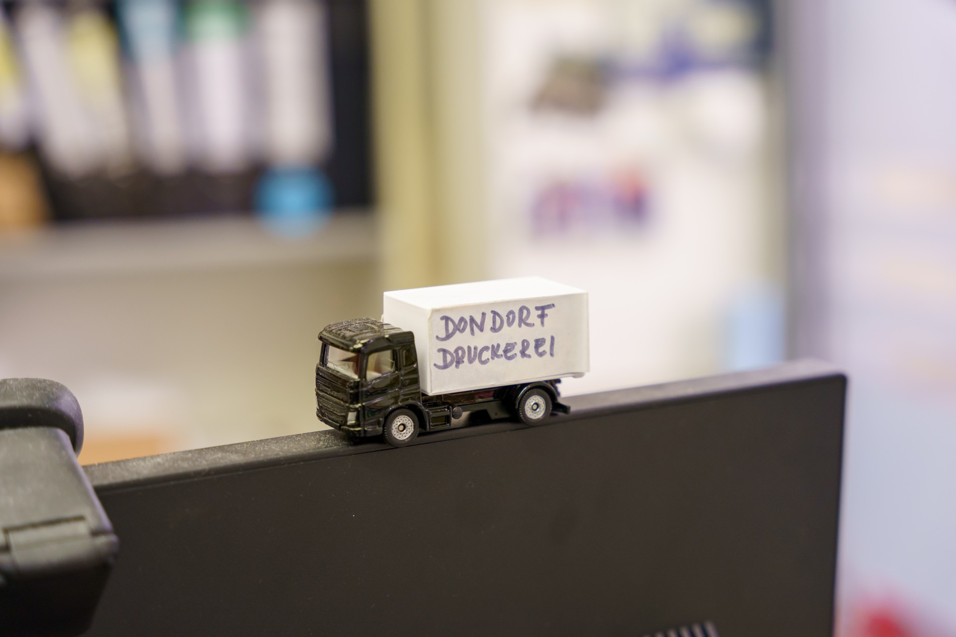 Miniatur-Lkw mit der Aufschrift „Dondorf Druckerei“ steht am Rand eines Bildschirms.