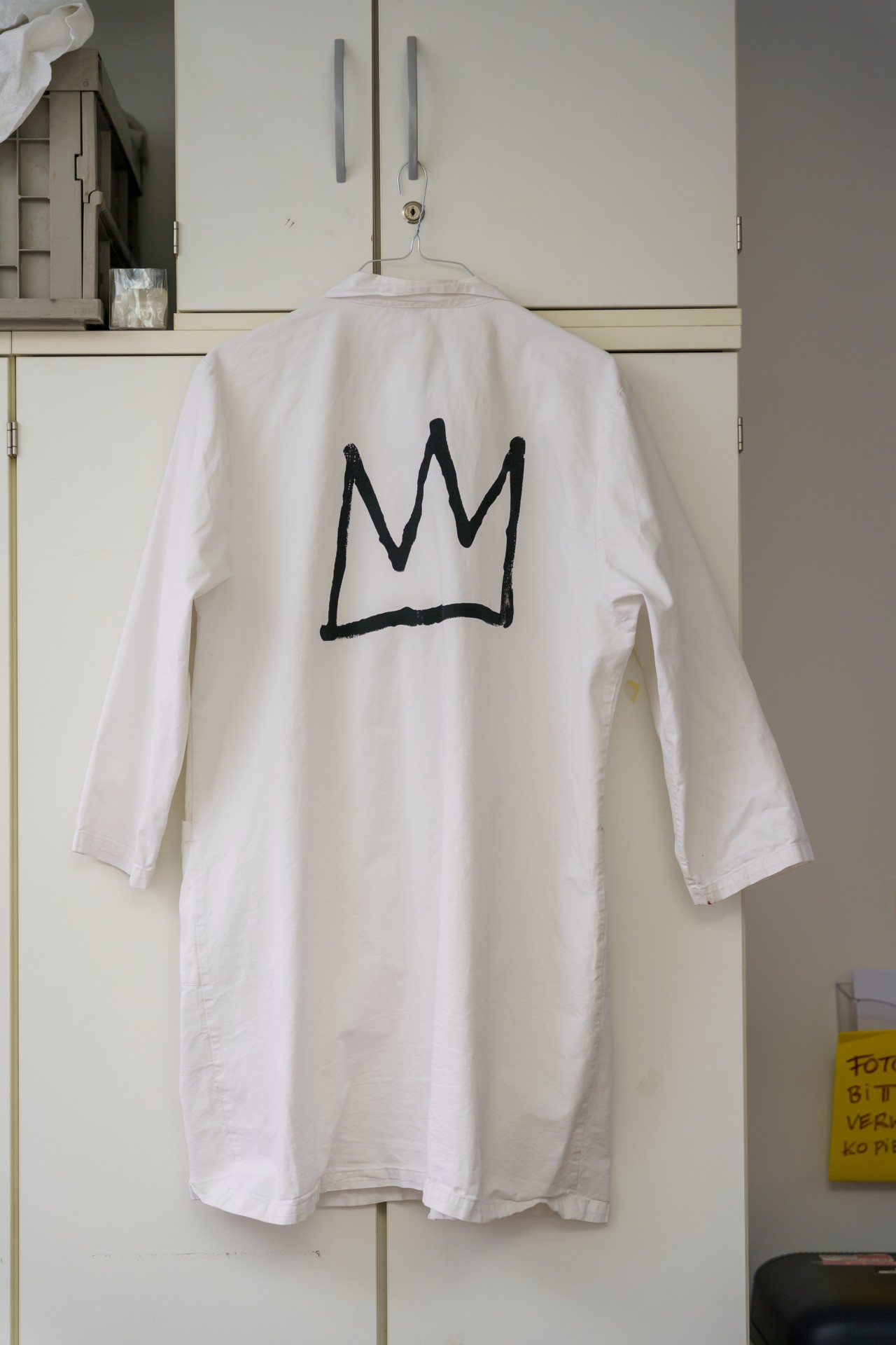 Weißes Hemd mit schwarzem Kronen-Motiv, an einem Schrank aufgehängt.