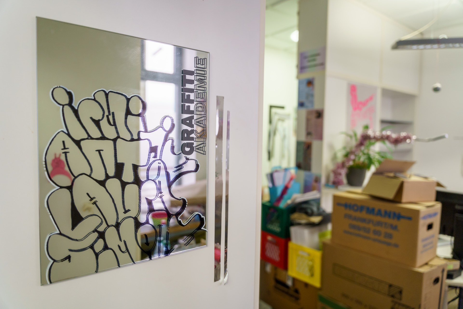 Spiegel mit Graffiti-Aufschrift "Graffiti Akademie", im Hintergrund Details eines kreativen Raums.