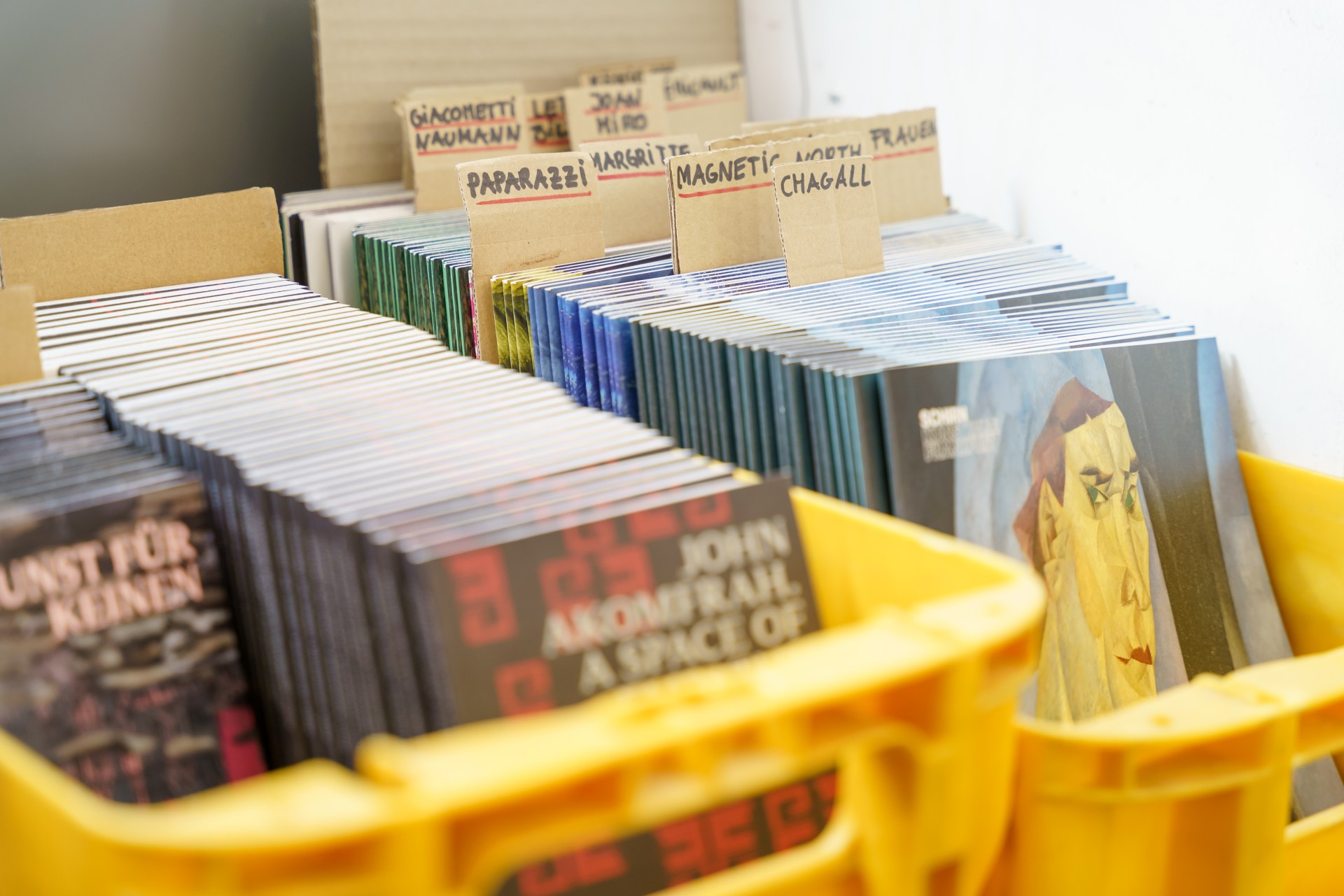 Ordner mit verschiedenen Zeitschriften und Katalogen, beschriftet mit Künstlernamen und Themen, in gelben Boxen.