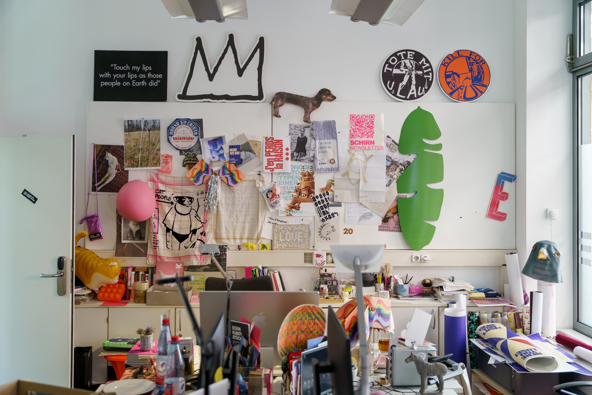 Bunt gestaltetes Arbeitszimmer mit Postern, Kunstwerken und kreativen Utensilien an Wand und Tisch.