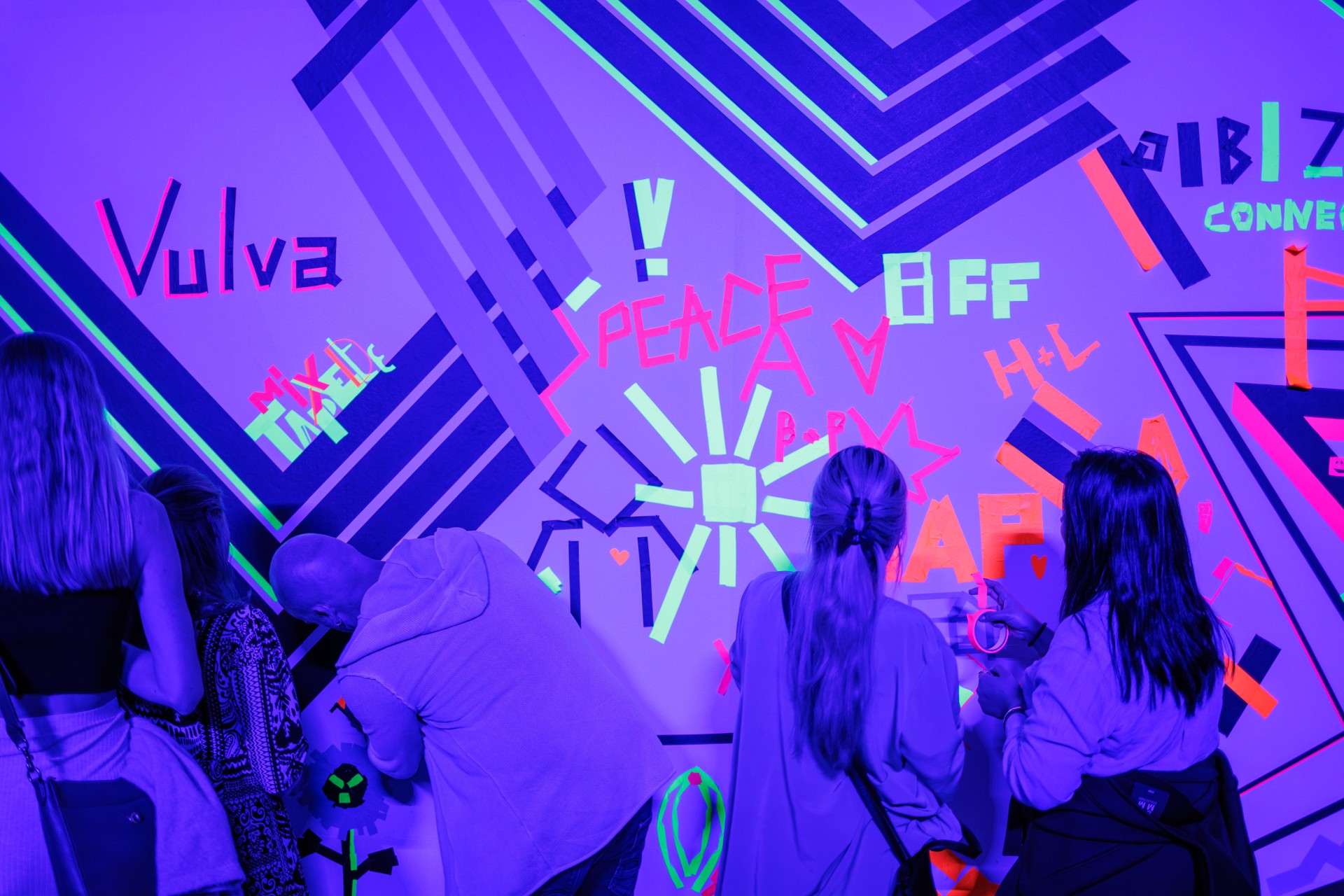 Menschen gestalten eine bunte Wand mit Neonaufklebern und Graffiti in einem kreativen Raum.