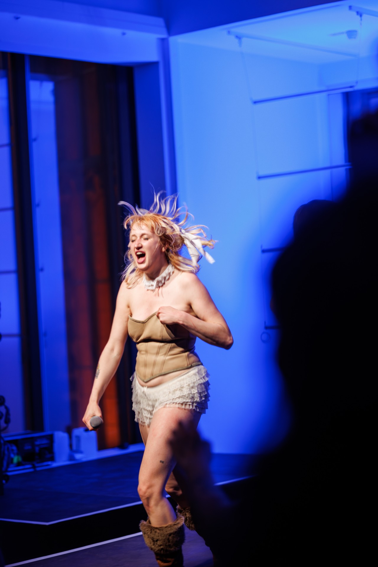 Frau mit blonden, bewegten Haaren singt auf einer Bühne und begeistert mit einer lebhaften Performance.