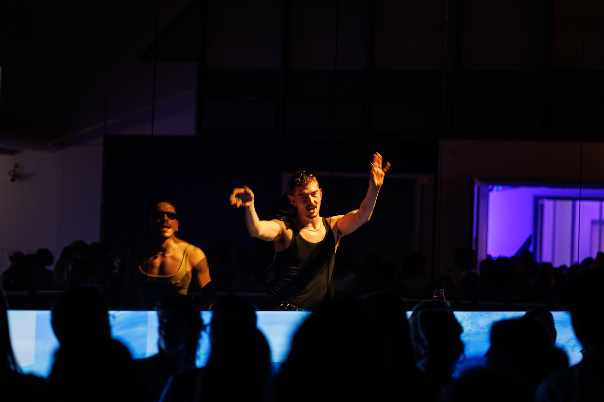 Zwei Performer auf der Bühne, umgeben von Publikum, während sie dynamisch Musik in einem Club-Setting vortragen.