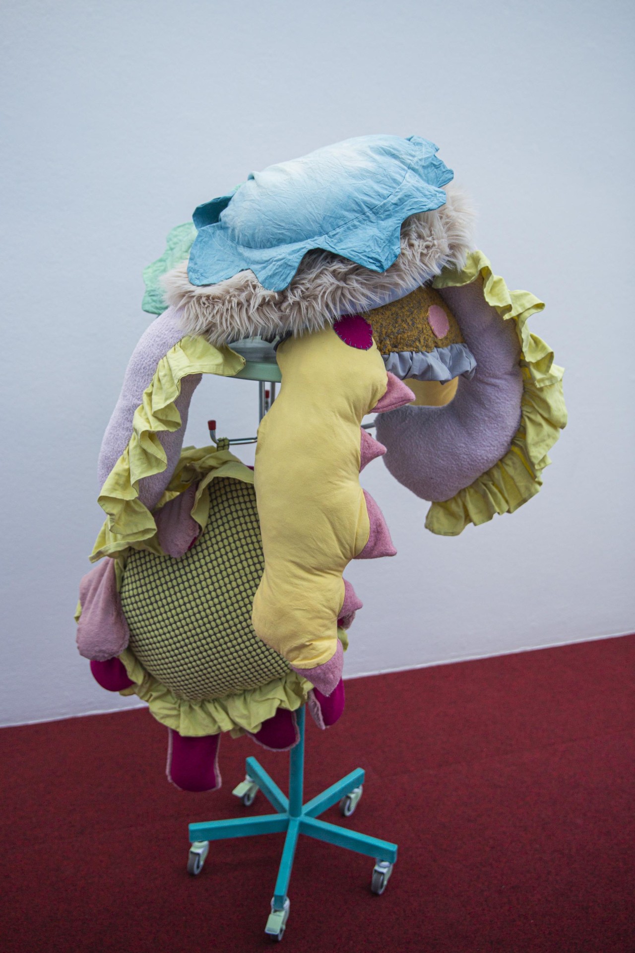 Bunt gestaltete textile Skulptur auf einem Ständer, vereint verschiedene Formen und Materialien.
