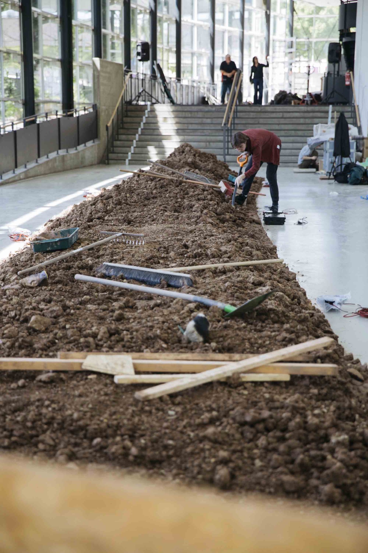 Person arbeitet an einem Erdhaufen in einem hellen Raum, umgeben von verschiedenen Werkzeugen.