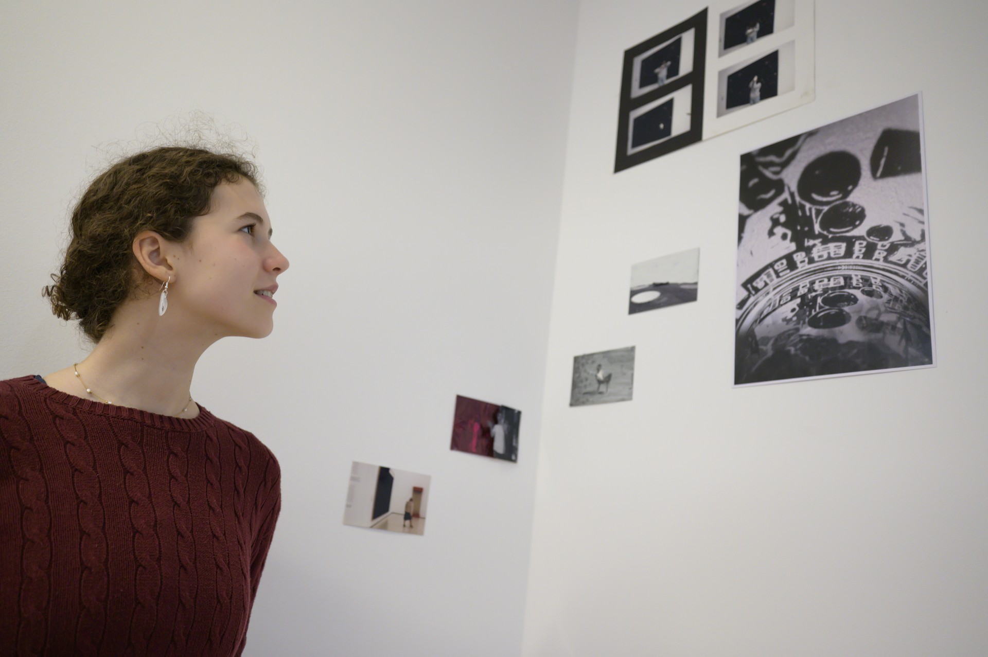 Junge Frau schaut sich Bilder an einer Wand an, umgeben von Fotos in einer kreativen Atmosphäre.