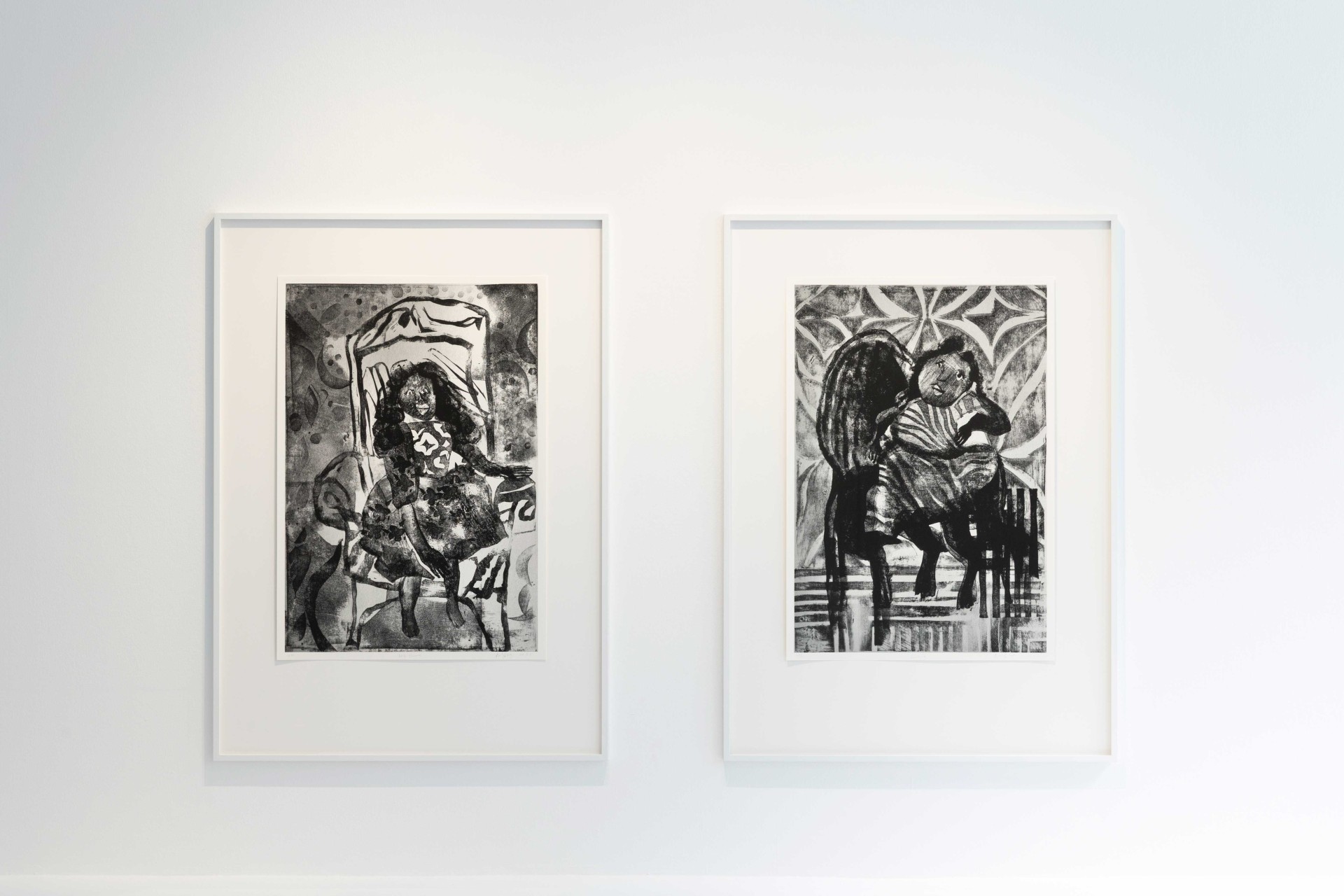 Two black and white artworks in frames depicting stylized figures sitting on chairs.