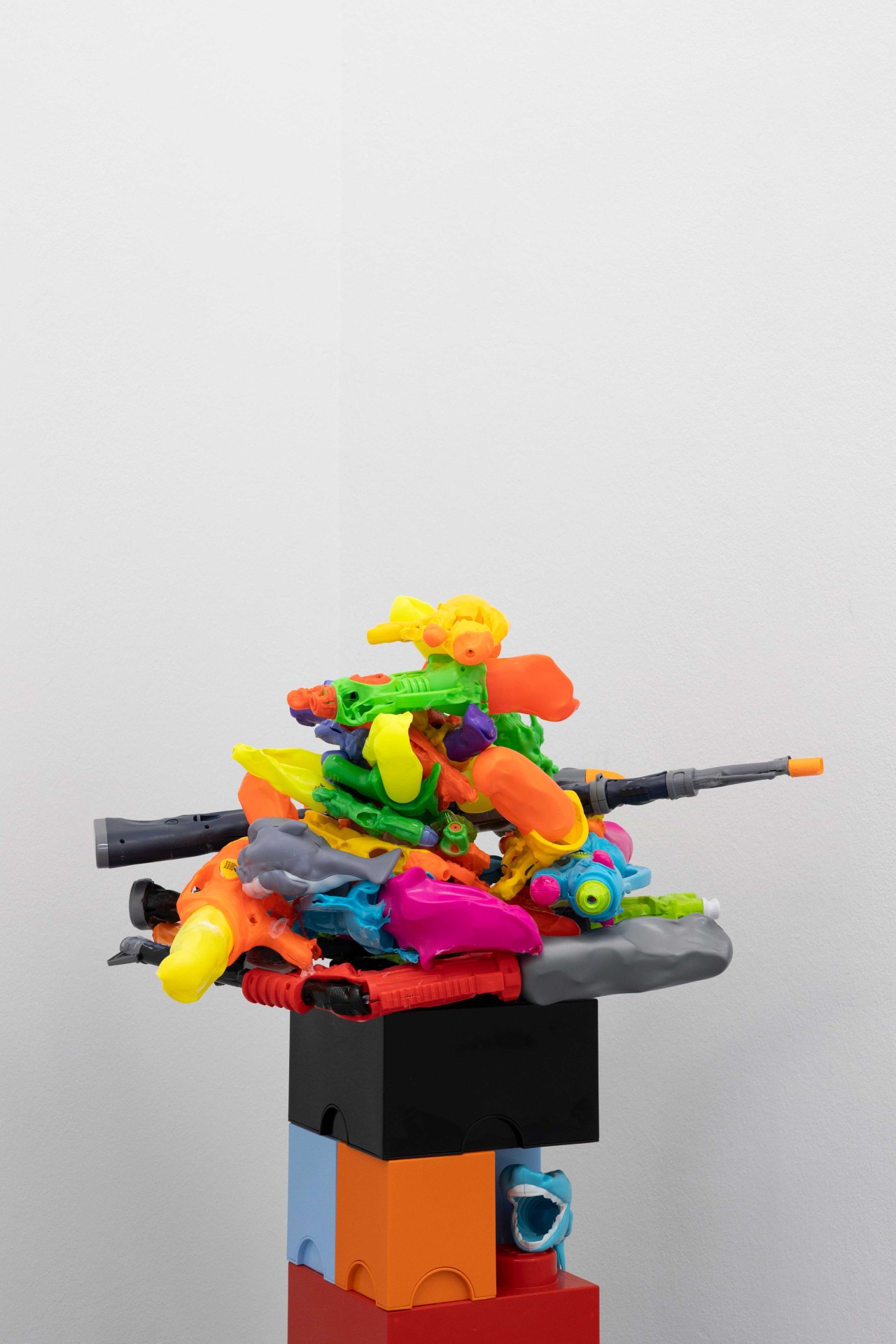 Colorful plastic toys are creatively stacked on a black box in front of a bright wall.