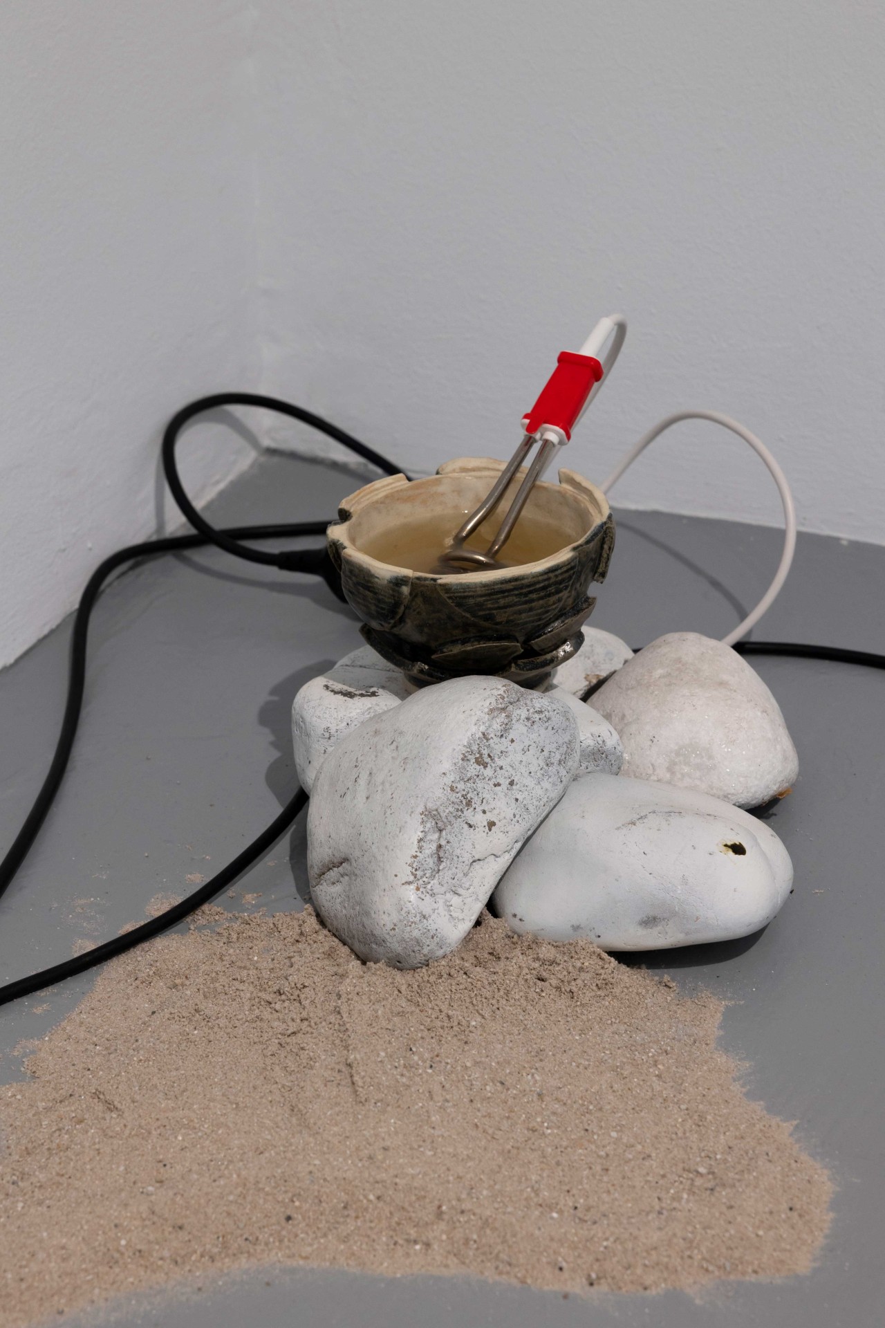 Artificial installation with a bowl, a heating device, stones, and sand in a corner.