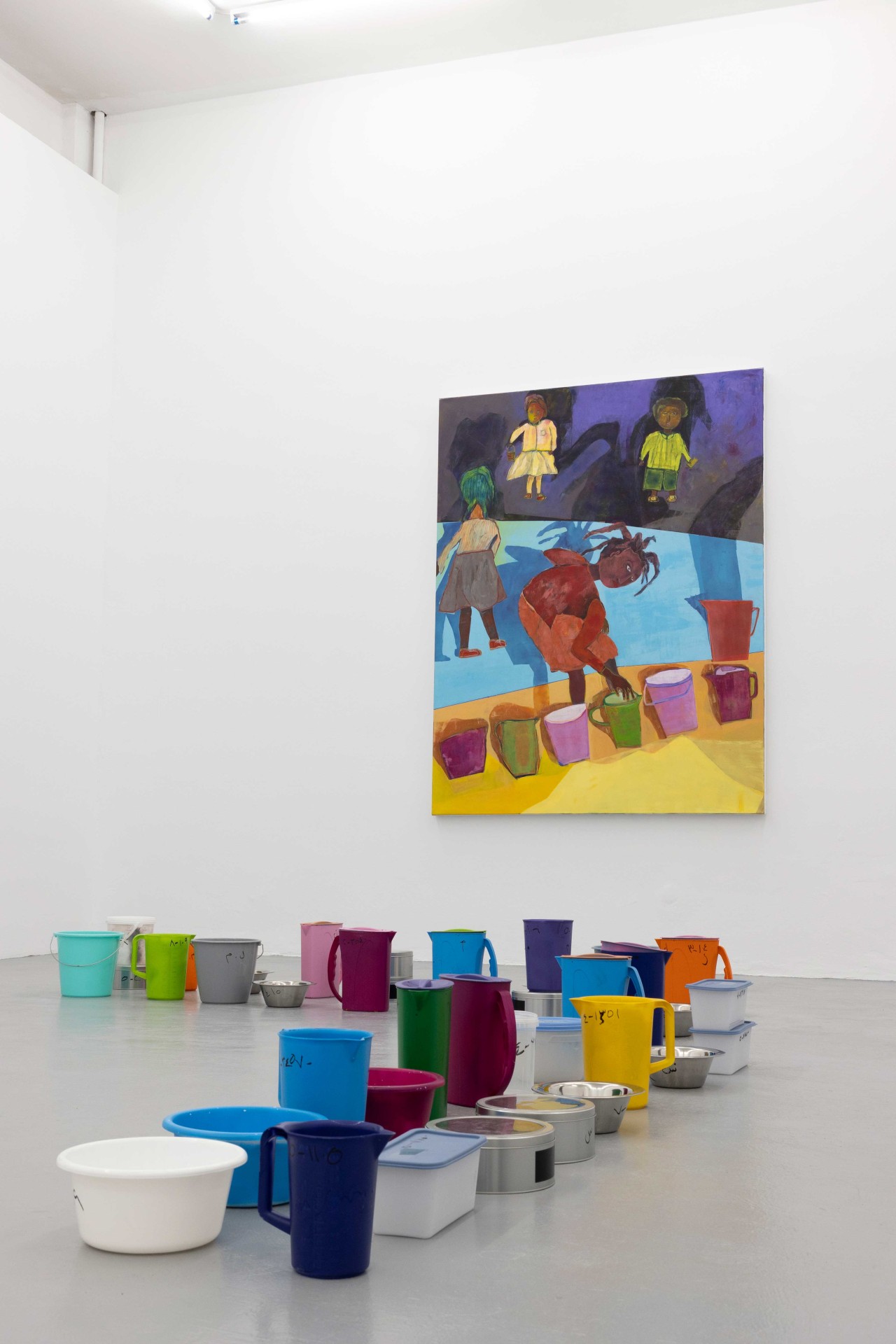 Colorful containers are in front of an artist's image in a minimalist gallery.
