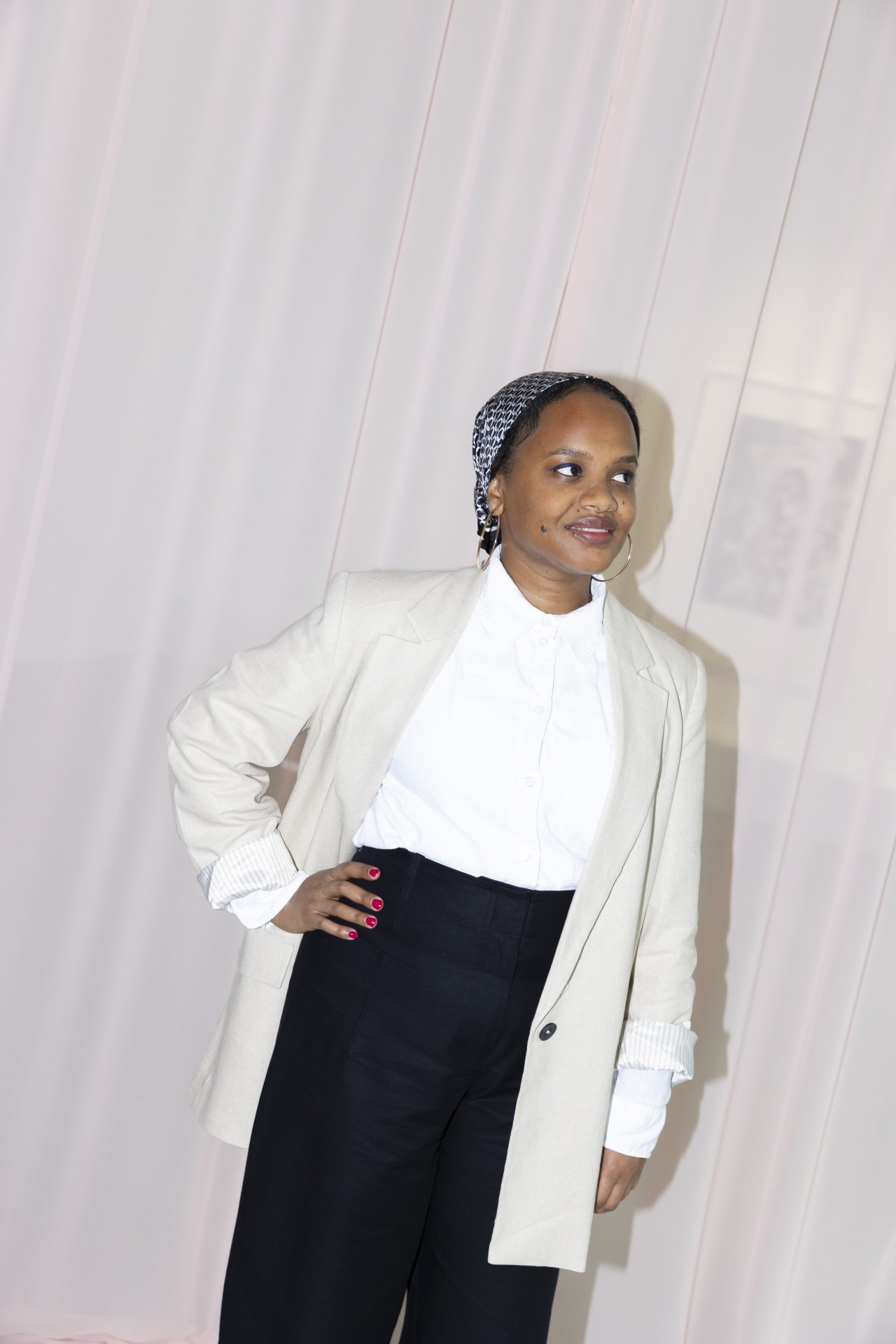Woman in a light jacket and black pants, smiling against a soft pink background.