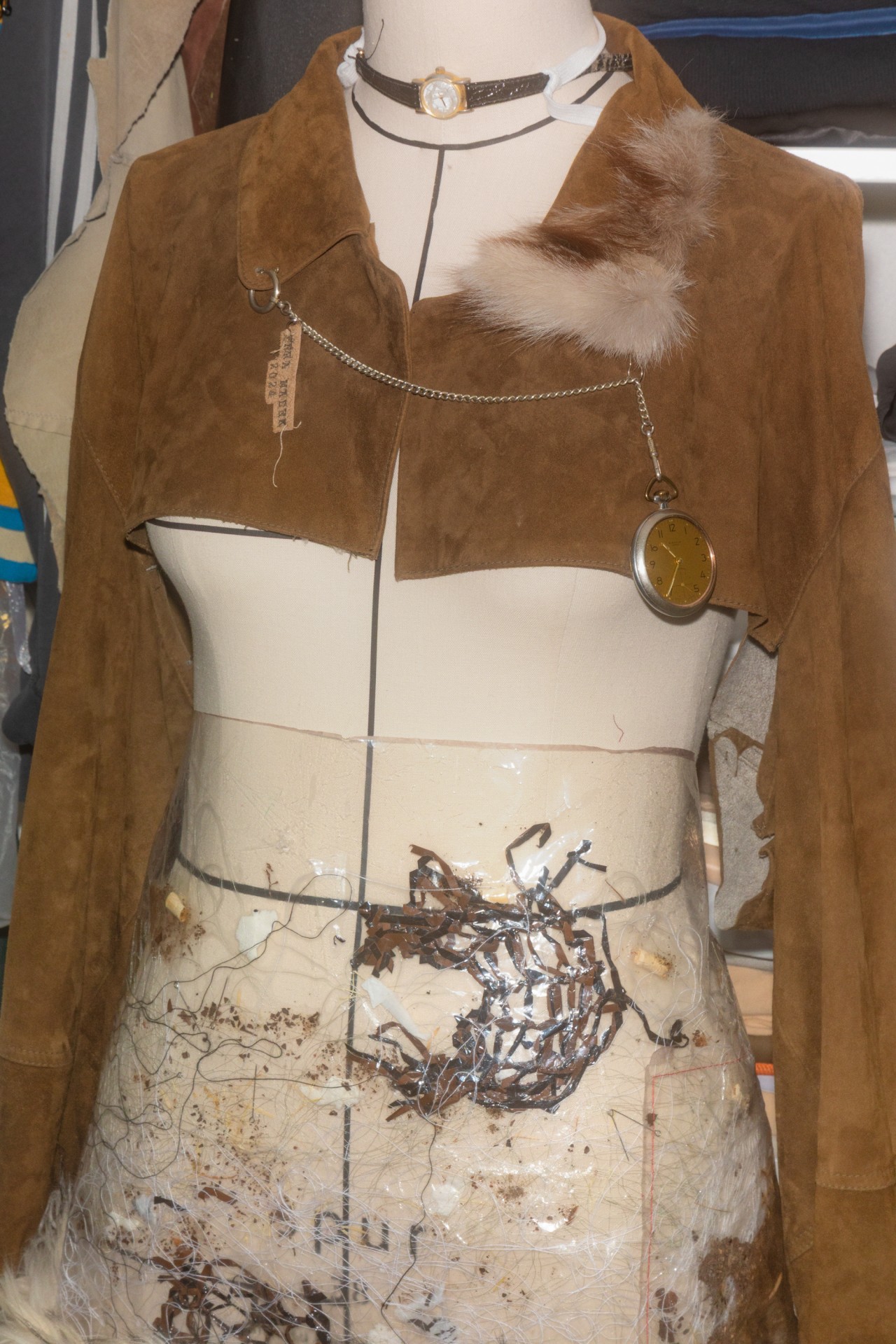 Braune Wildlederjacke mit Fellkragen und Kette, dekoriert mit Taschenuhr und verschiedenen Textilien am Mannequin.