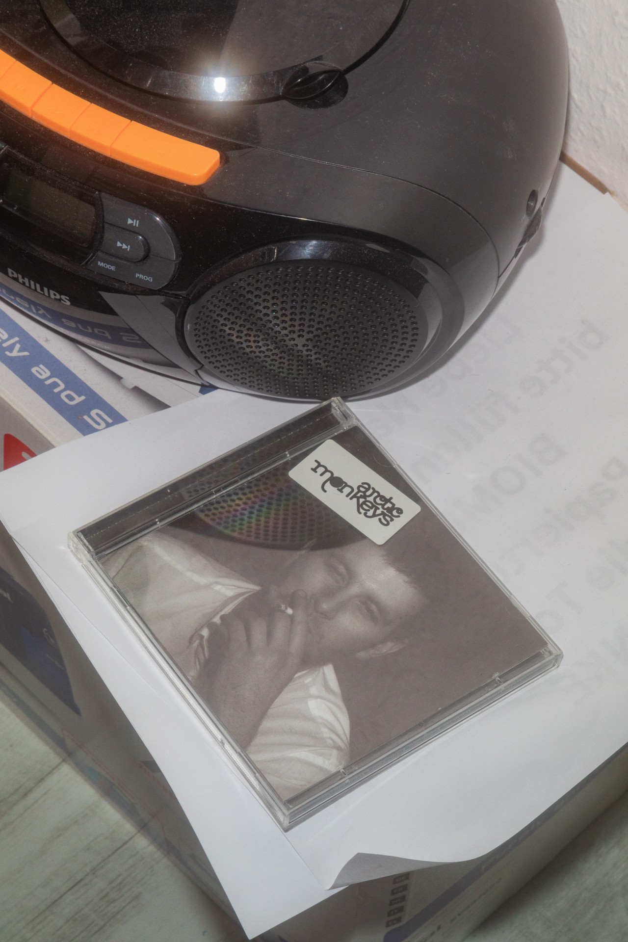 CD-Cover der Arctic Monkeys liegt neben einem tragbaren CD-Player auf einem Papierstapel.