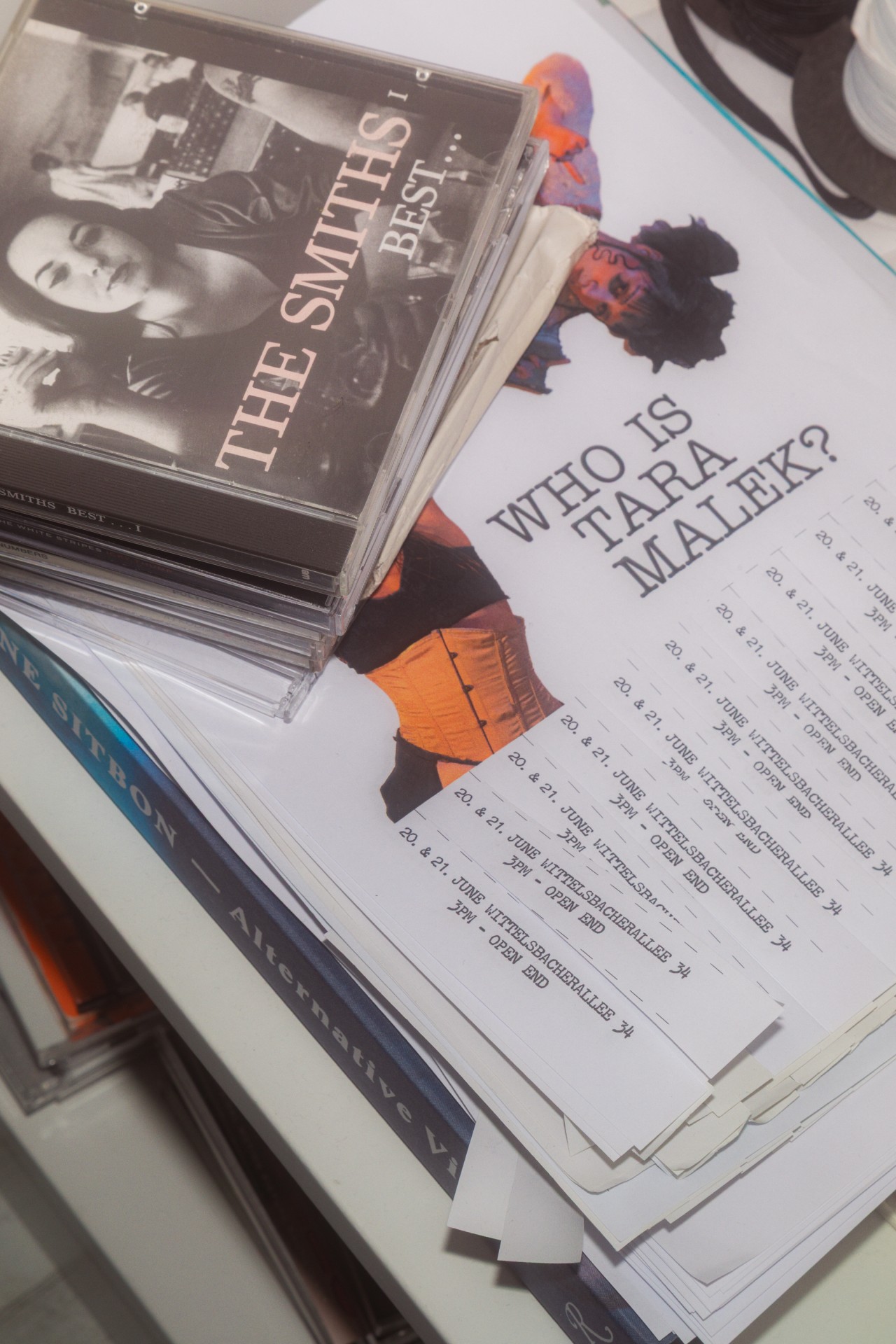 CDs von The Smiths und ein Veranstaltungsflyer mit der Frage "Wer ist Tara Malek?" liegen auf einem Tisch.