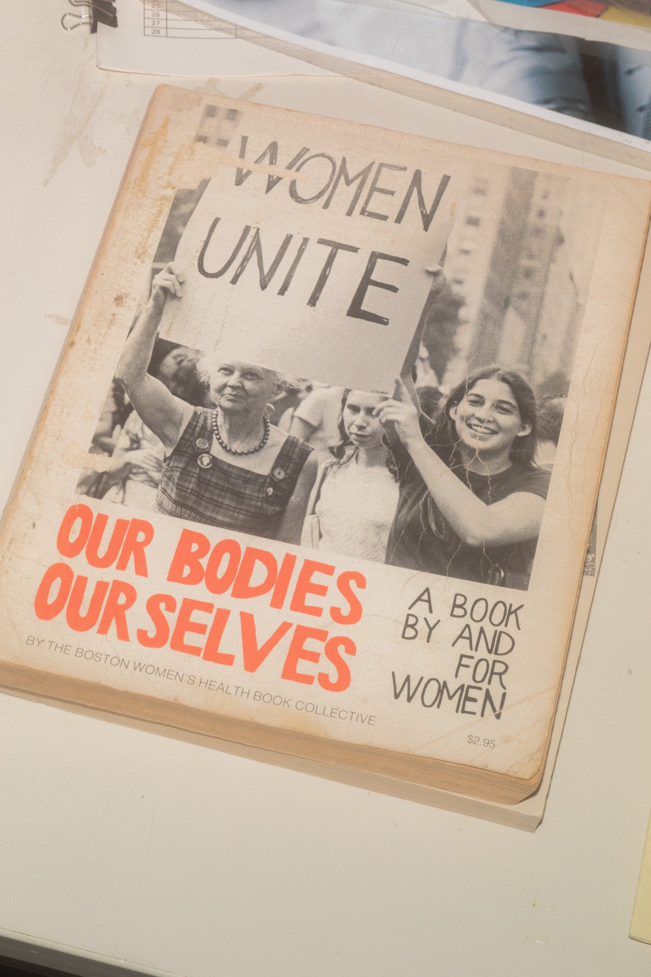 Buchcover mit dem Titel „Unsere Körper, unser Selbst“ und Frauen, die ein Schild mit „Frauen vereint“ halten.