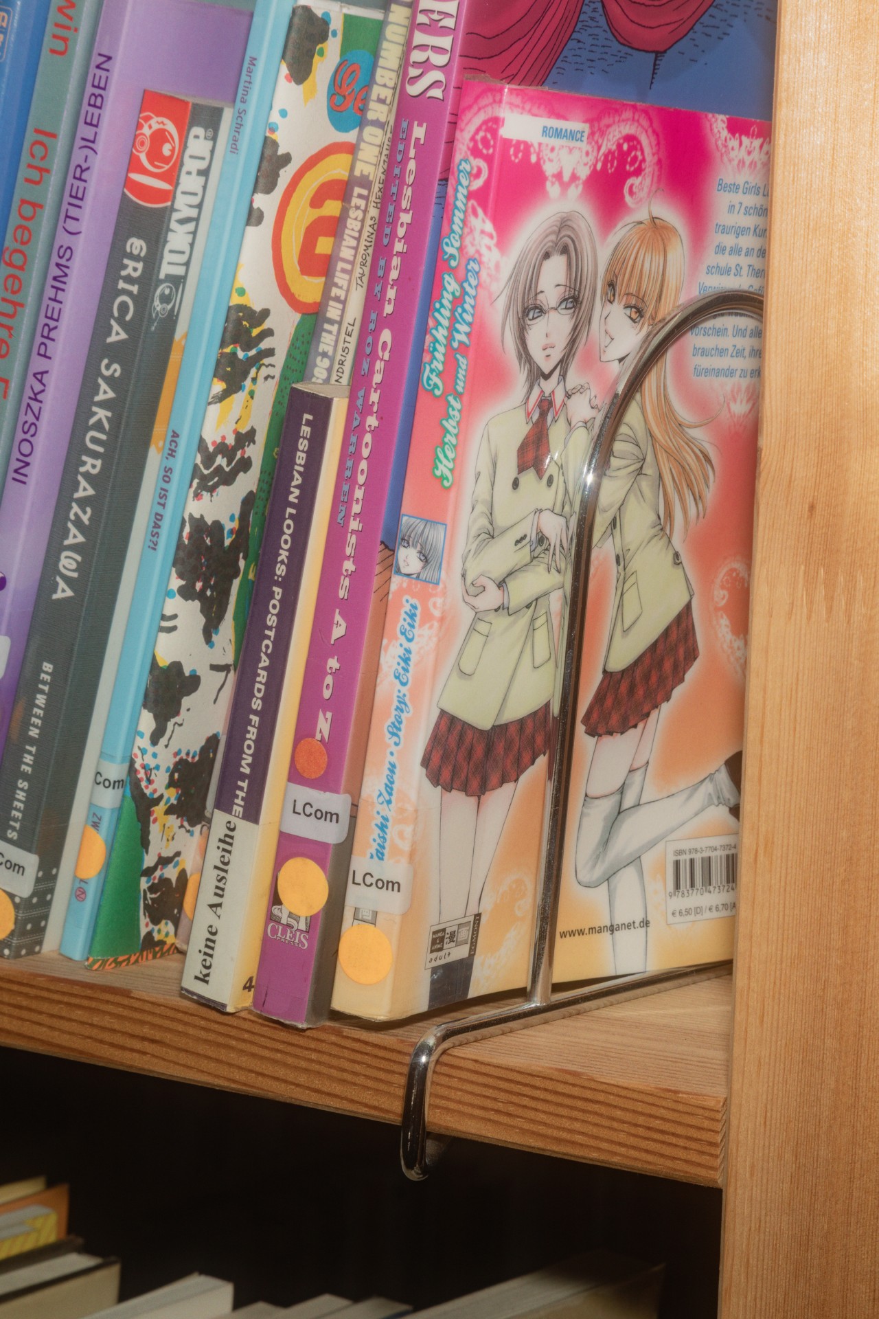 Bücherregal mit verschiedenen Comics und Mangas, darunter auch lesbische Themen und Illustrationen.