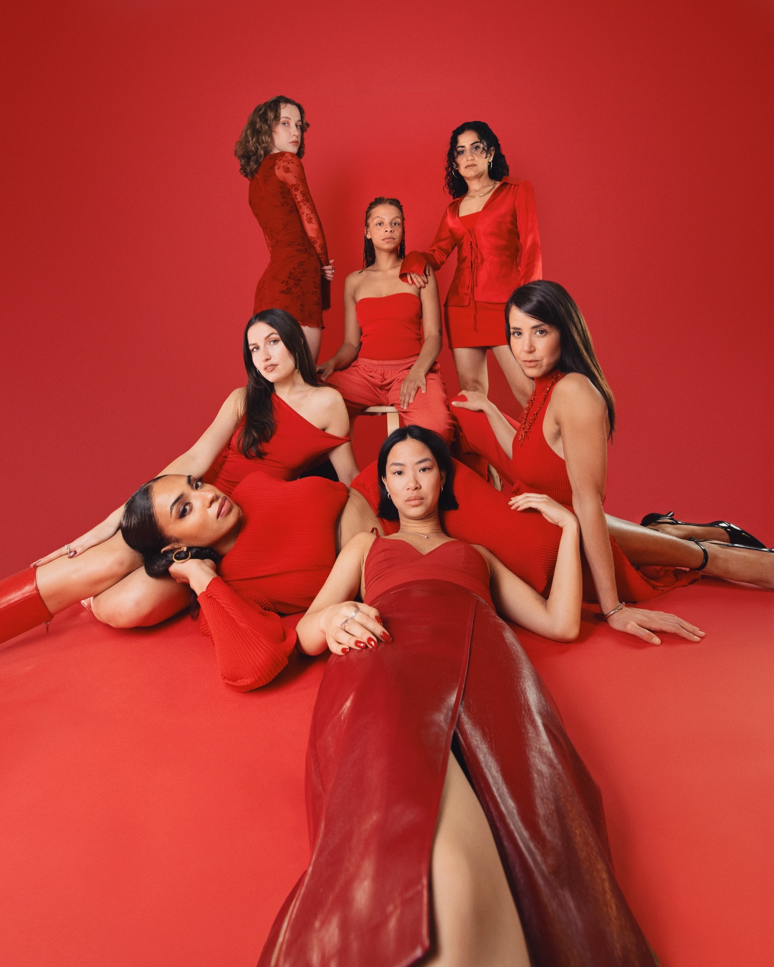 Gruppierung von sieben Frauen in roten Outfits vor rotem Hintergrund, posierend für ein modisches Fotoshooting.