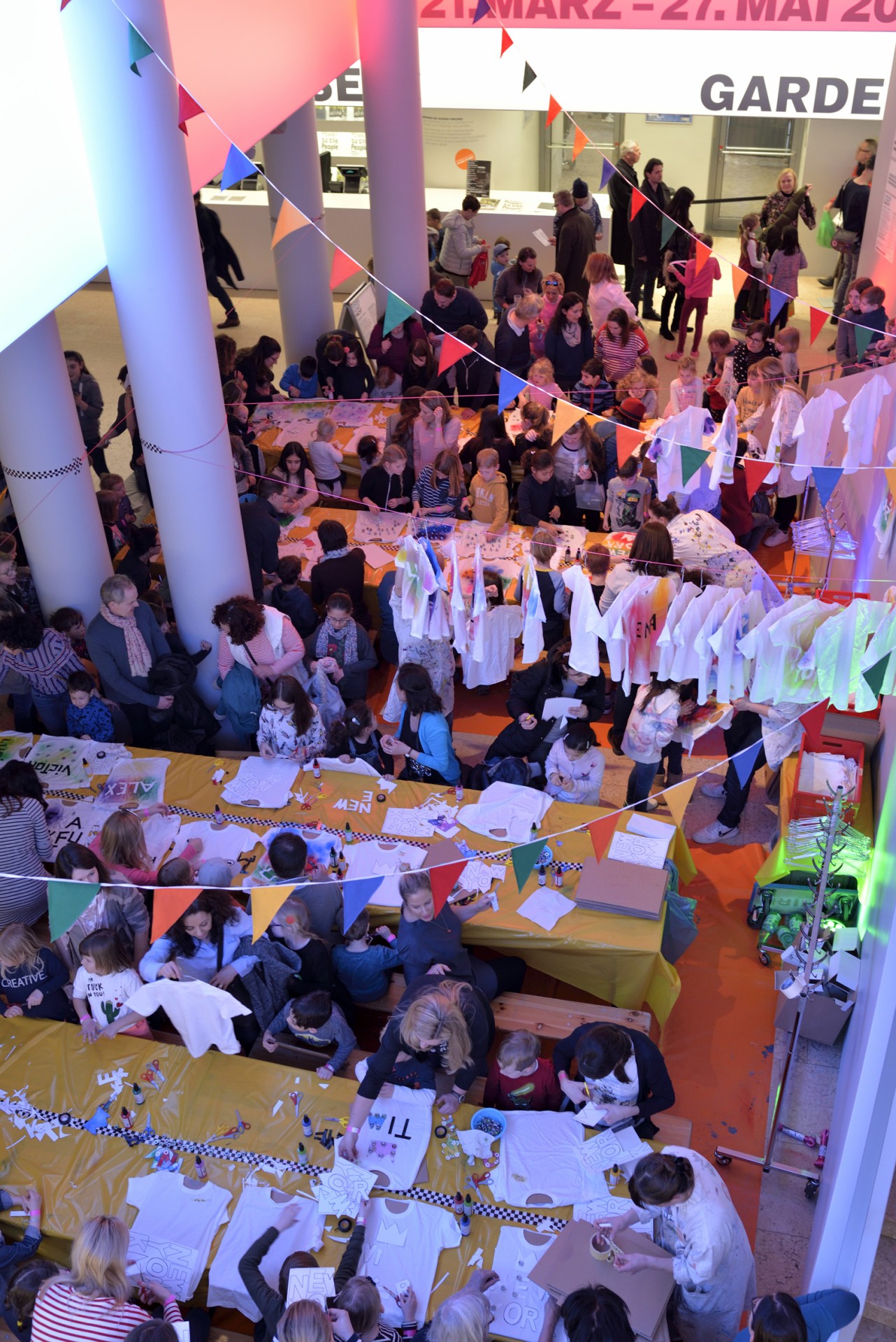 Colorful children's event with craft tables, T-shirt designs, and a cheerful atmosphere decorated with bunting.