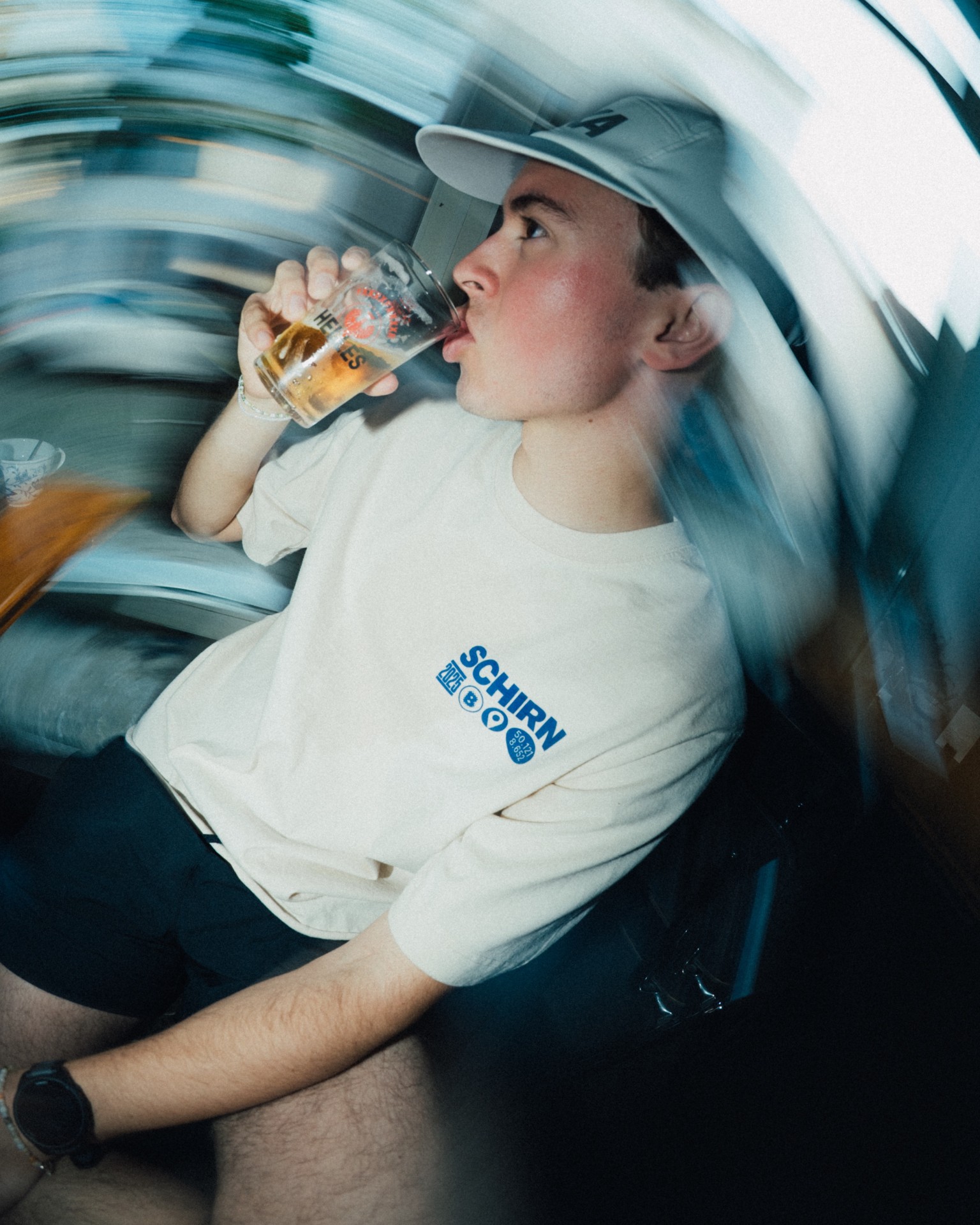 Junger Mann mit Cap trinkt ein Glas Bier vor einem Hintergrund aus bewegten Farben. Entspannte Atmosphäre.