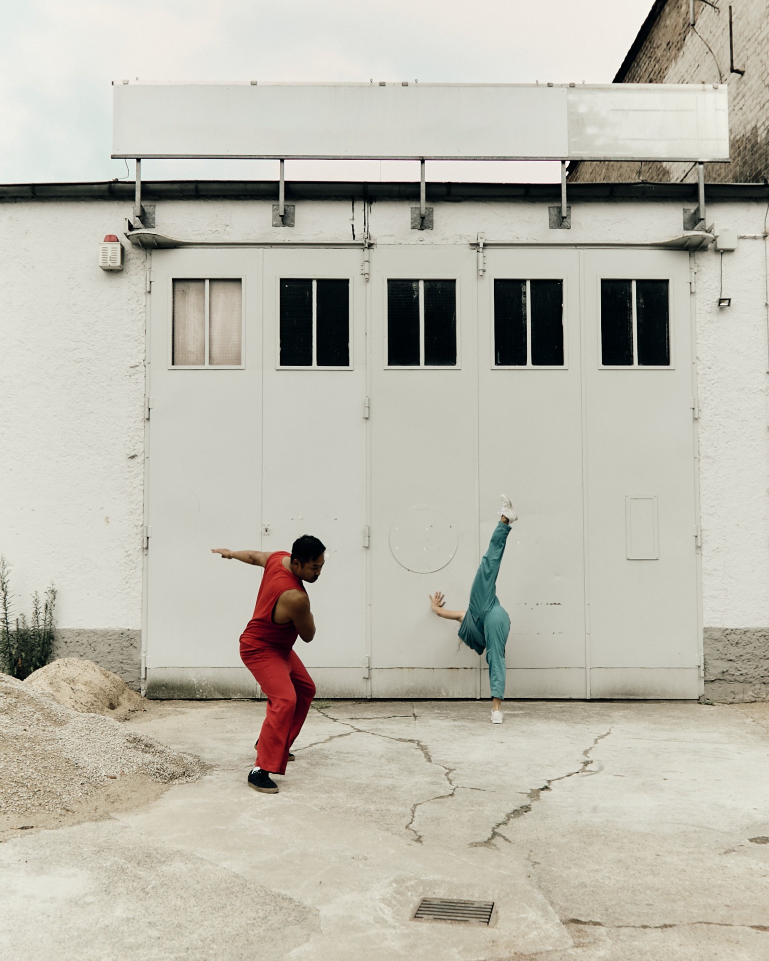 Tanzende Personen vor einer grauen Wand, einer in Rot, der andere in Blau, in dynamischer Pose.