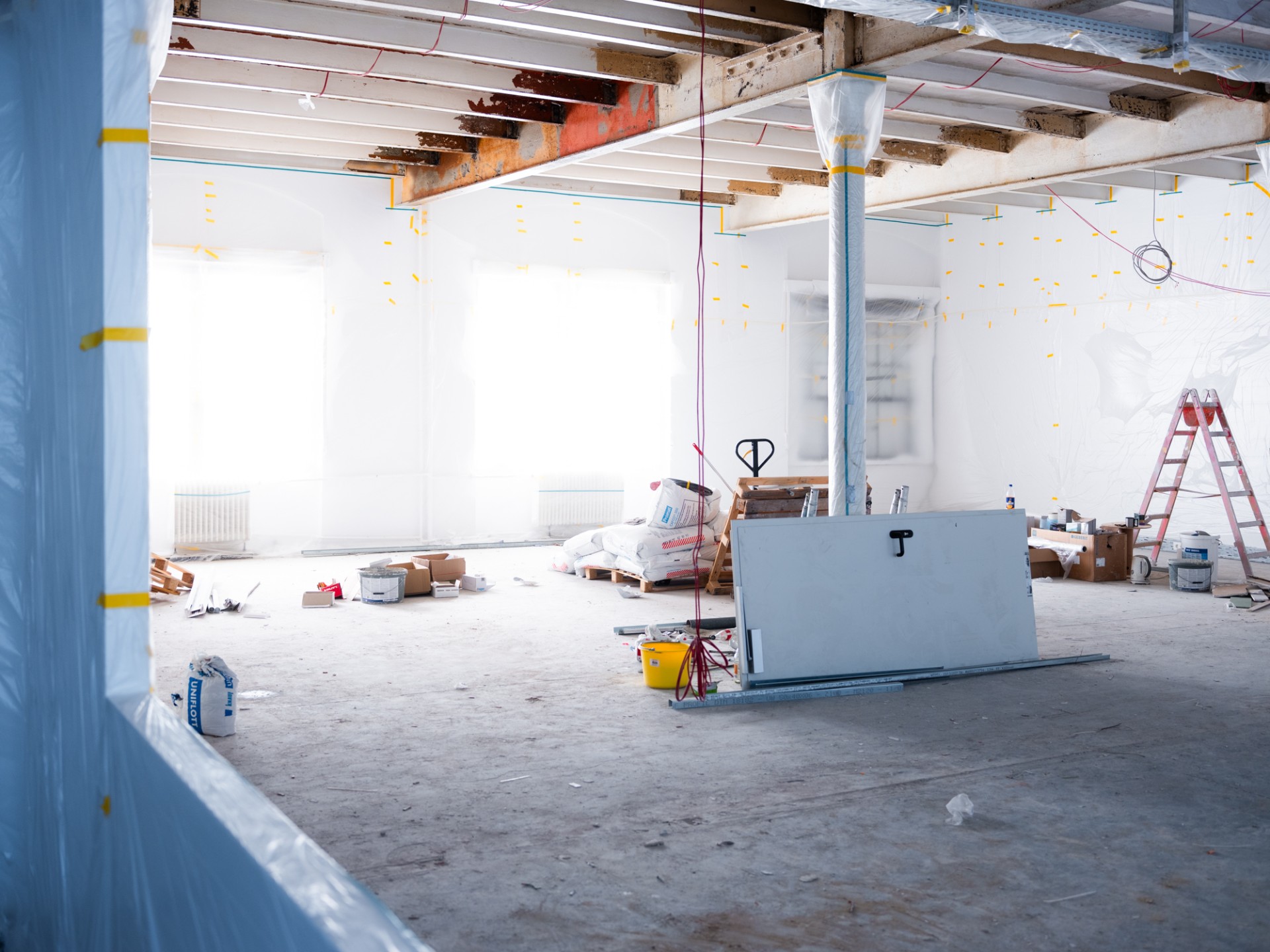 Leeres, unordentliches Zimmer mit Baustellenmaterial und sichtbaren Renovierungsarbeiten an Wänden und Decke.