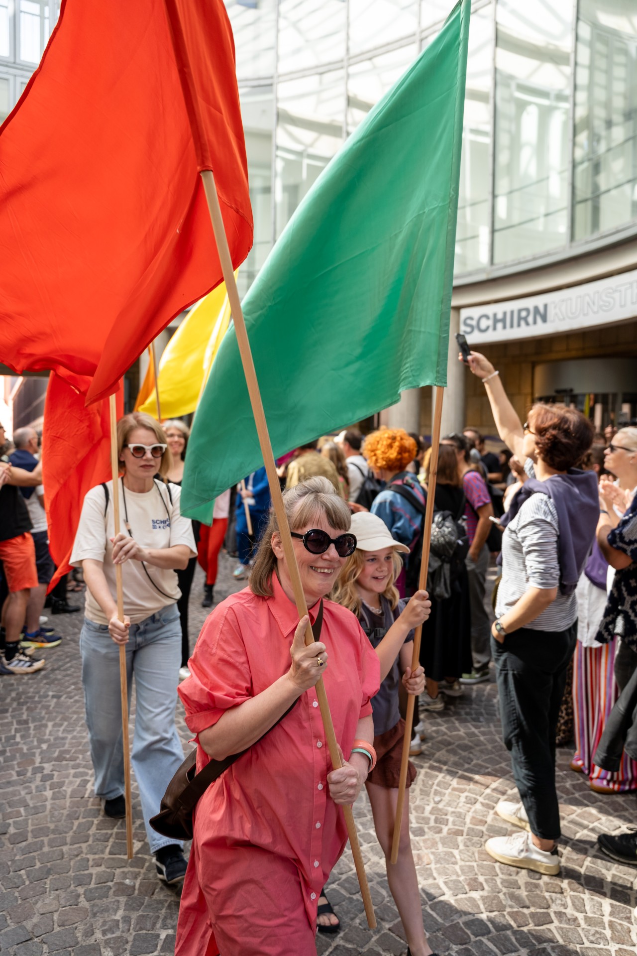 Menschen feiern in einer belebten Straße und schwenken bunte Fahnen während einer Veranstaltung.