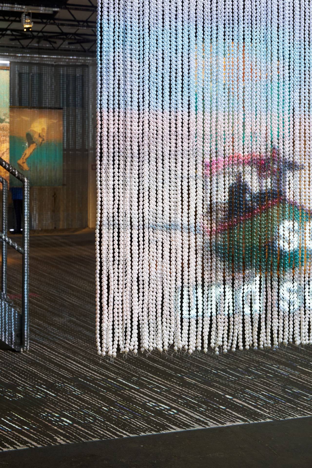 Partition made of beads, colorful light reflections, artwork in the background in a modern exhibition space.