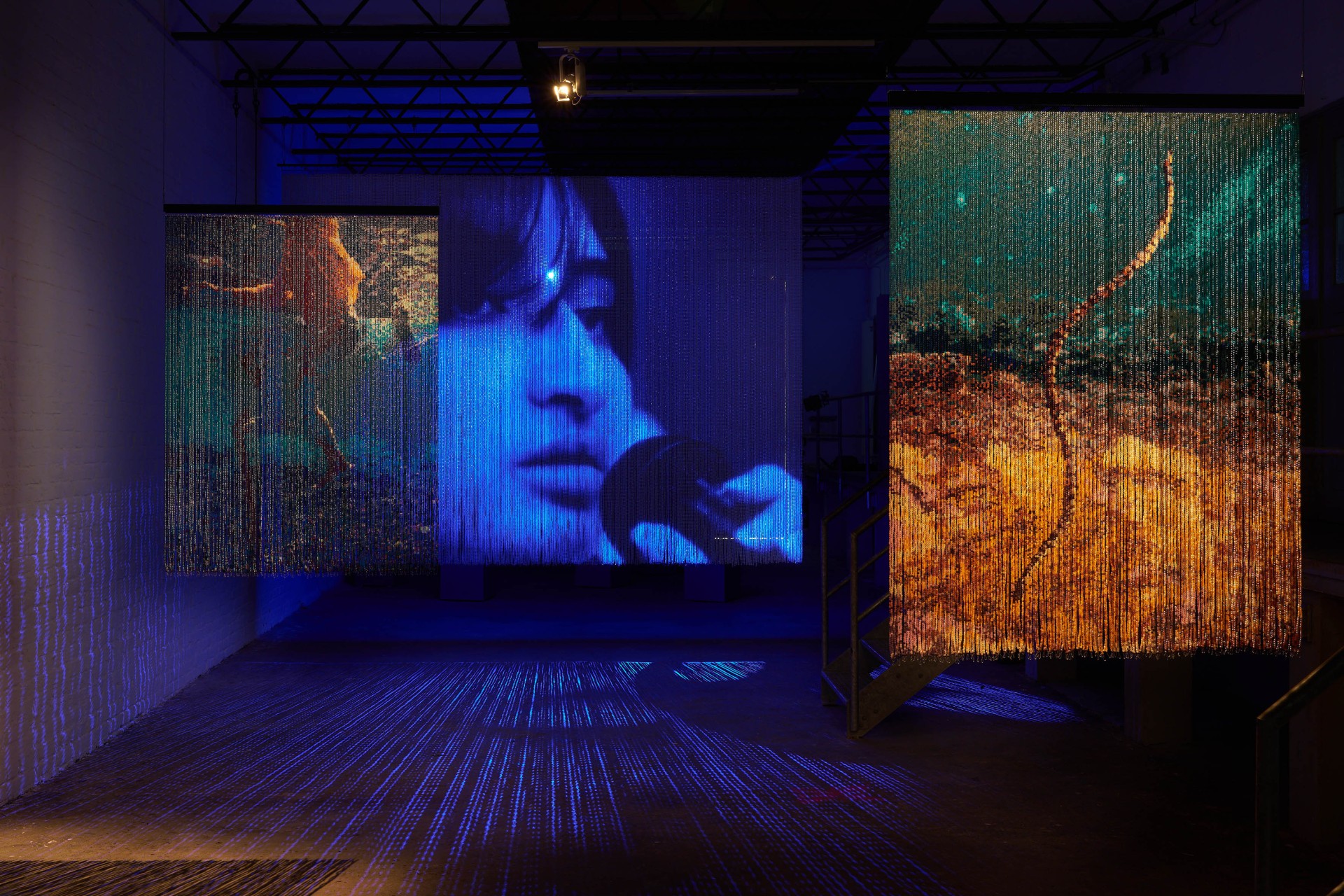 Installation with transparent curtains displaying images and faces in shades of blue and orange.
