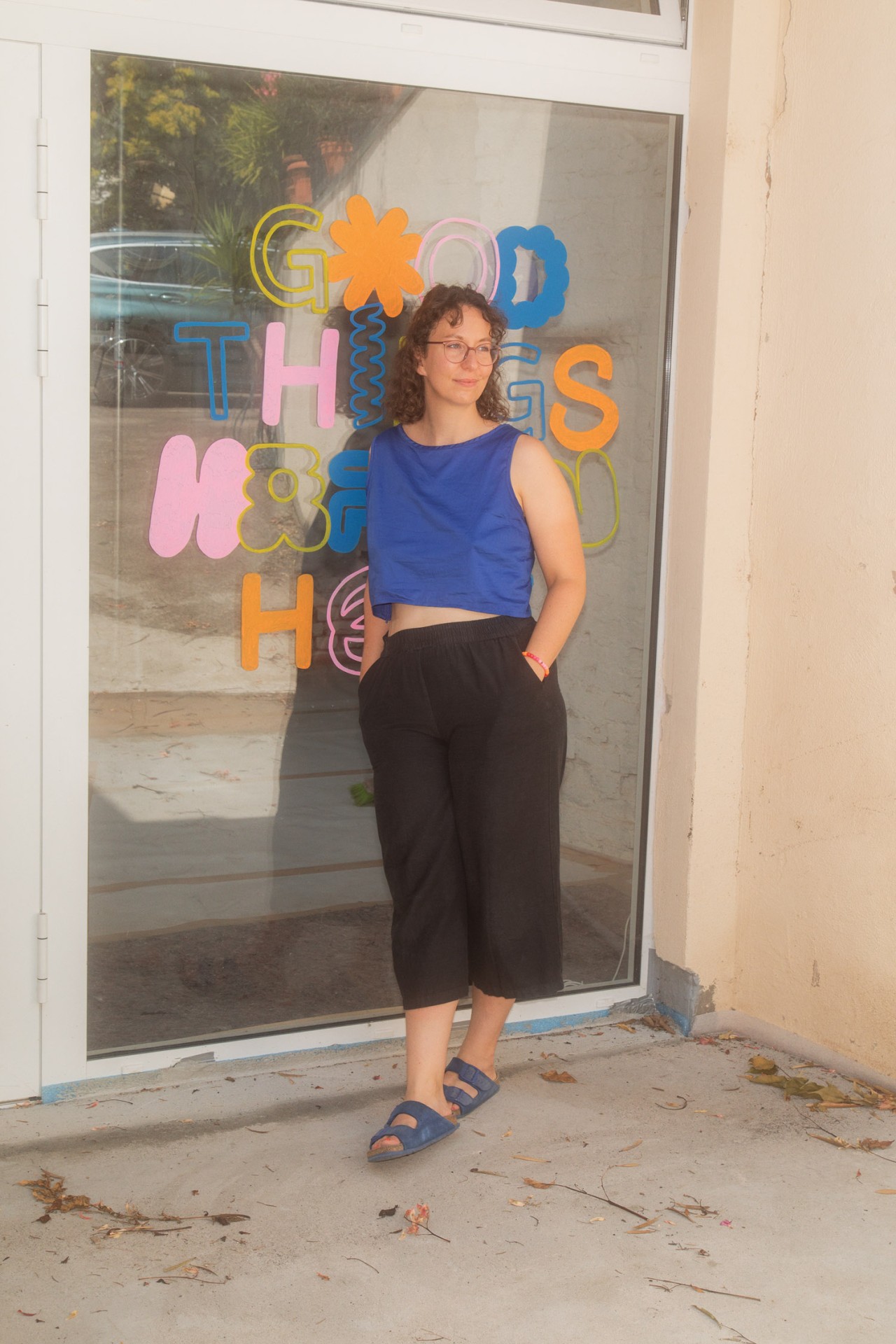 Junge Frau steht vor einem Fenster, auf dem bunte Buchstaben "Good Things Happen" in urbaner Umgebung formen.