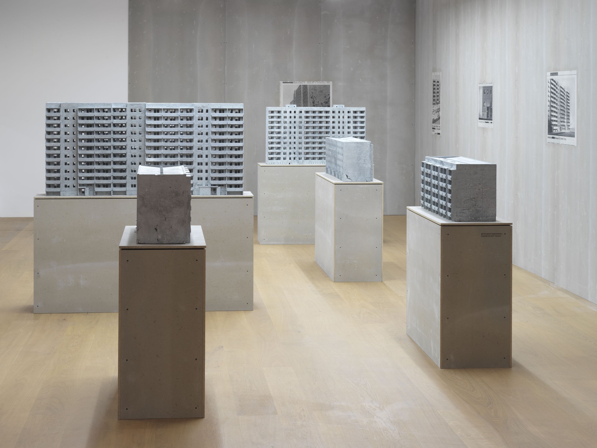 Moderne Ausstellung mit miniaturisierten Betonmodellen von Wohngebäuden auf Sockeln in einem minimalistischen Raum.