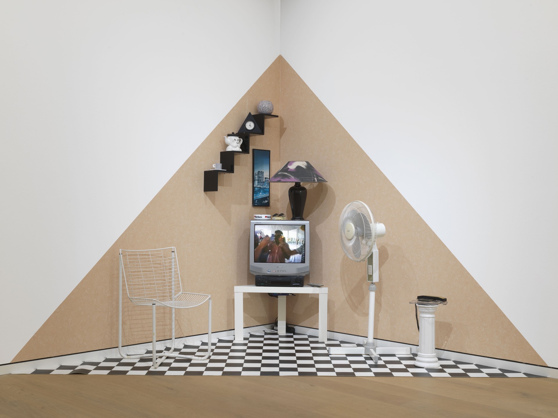 Ein kreativer Raum mit Fernsehecke, Ventilator, Lampe und geometrischen Wänden in neutralen Farben.