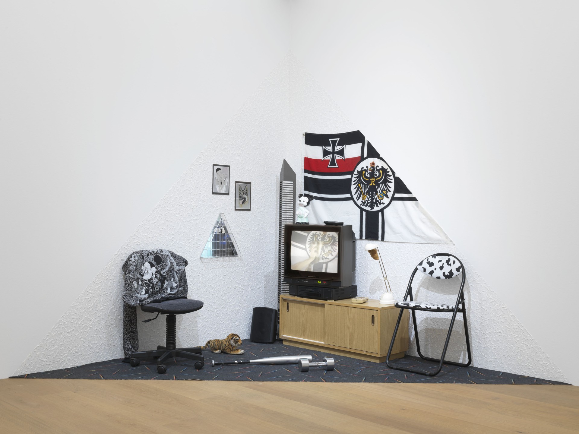 Eine moderne Ecke mit Möbeln, einer Flagge, Bildern und einem Fernseher in einem minimalistischen Raum.