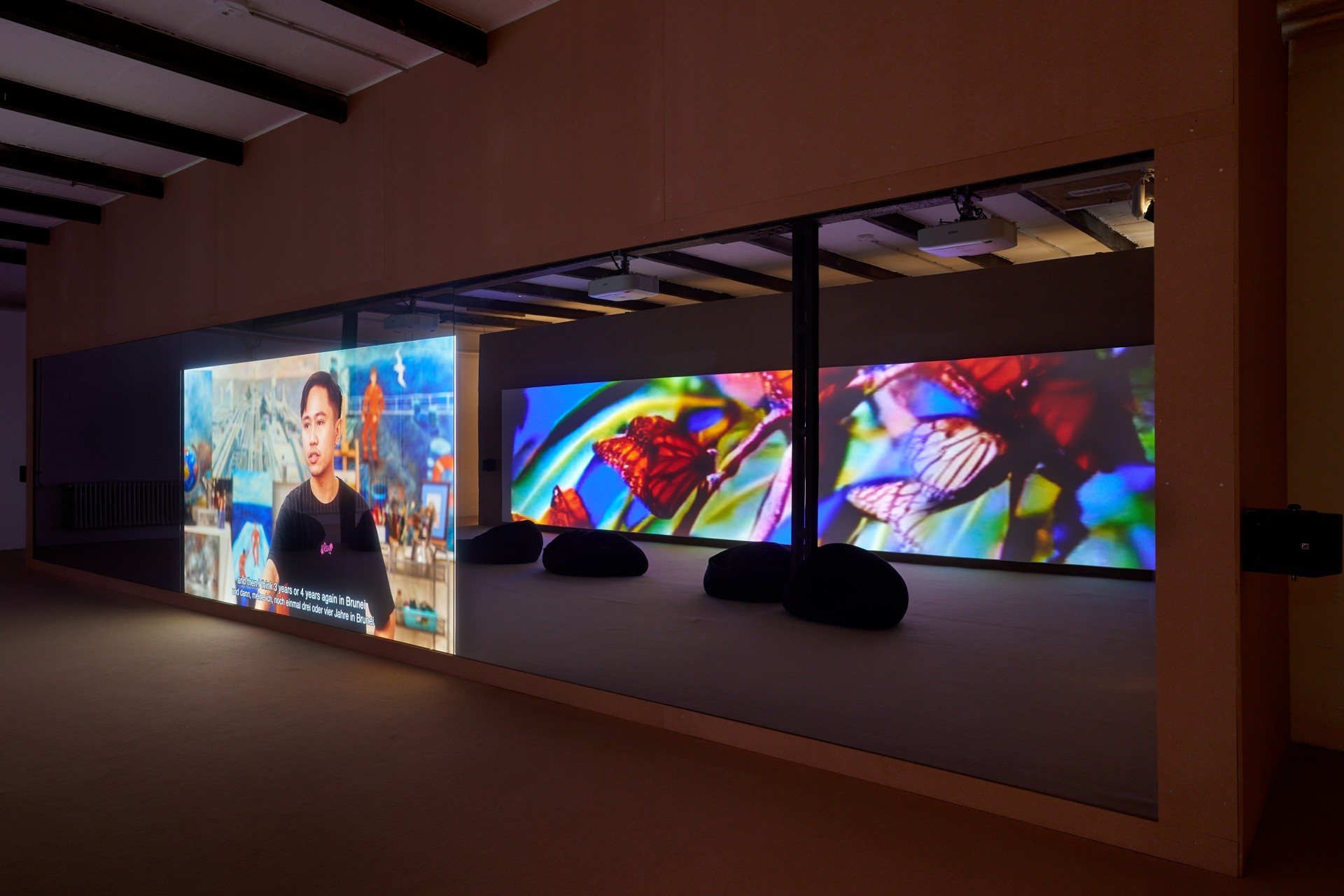 Multimedia installation with videos and colorful projections in a room, visible seating is arranged.