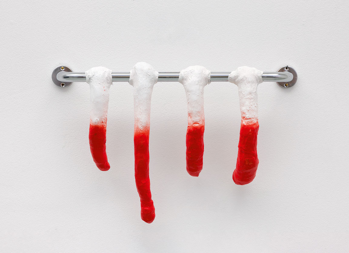 Rote, tropfende Skulpturen hängen an einer Stange vor einer weißen Wand, die an Knochen erinnert.
