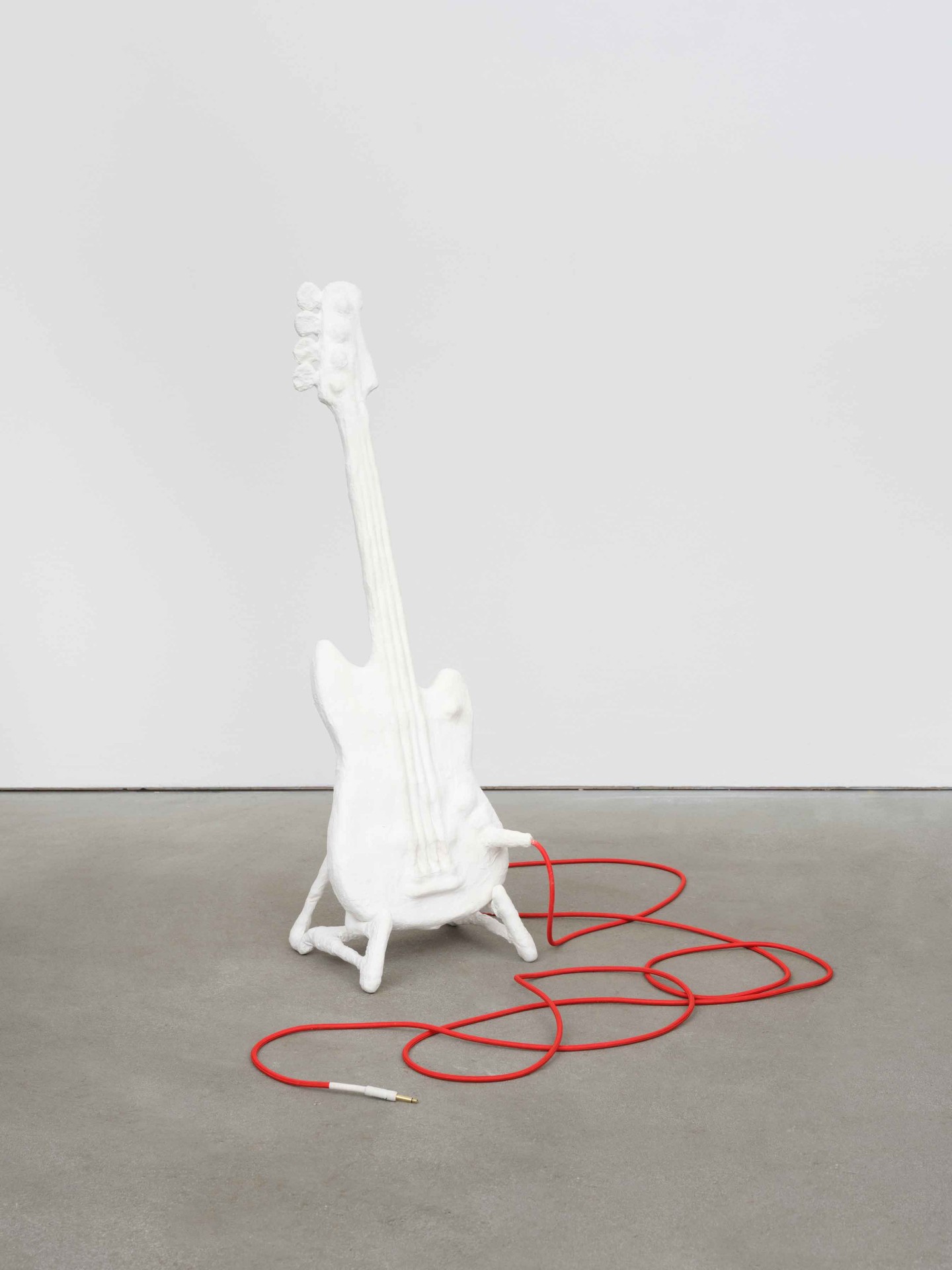Weiße Gitarre mit rotem Kabel auf grauem Boden, ein Kunstobjekt mit minimalistischer Ästhetik.