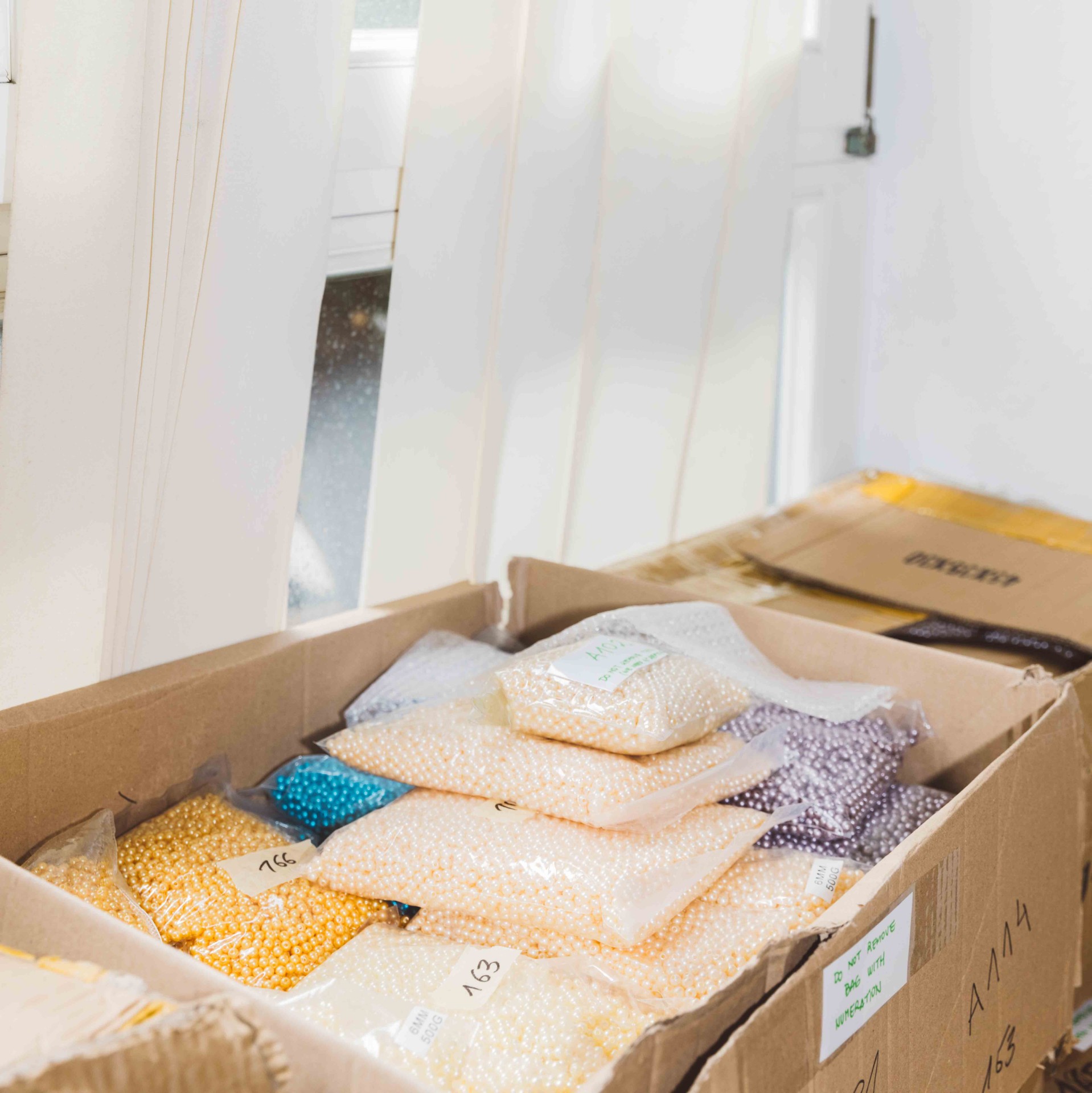 A box with various bags of beads in different colors, in front of a window letting in light.