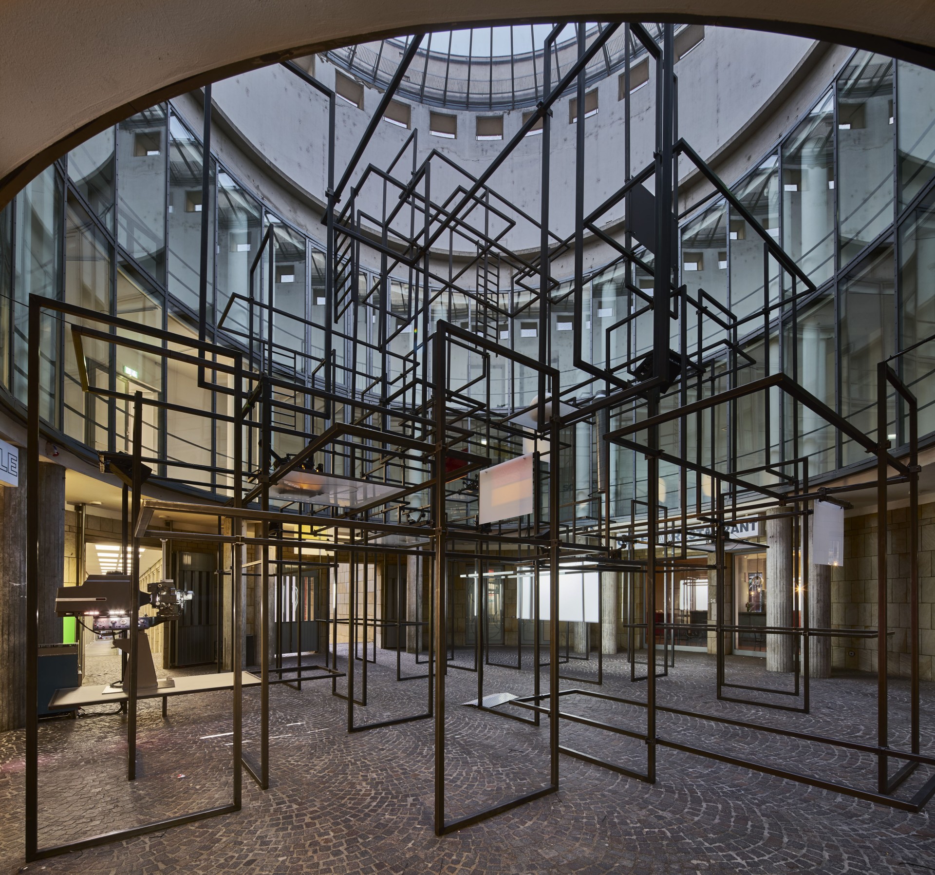 Moderne Installation aus schwarzgerahmten Strukturen in einem lichtdurchfluteten Raum mit Glaswänden.