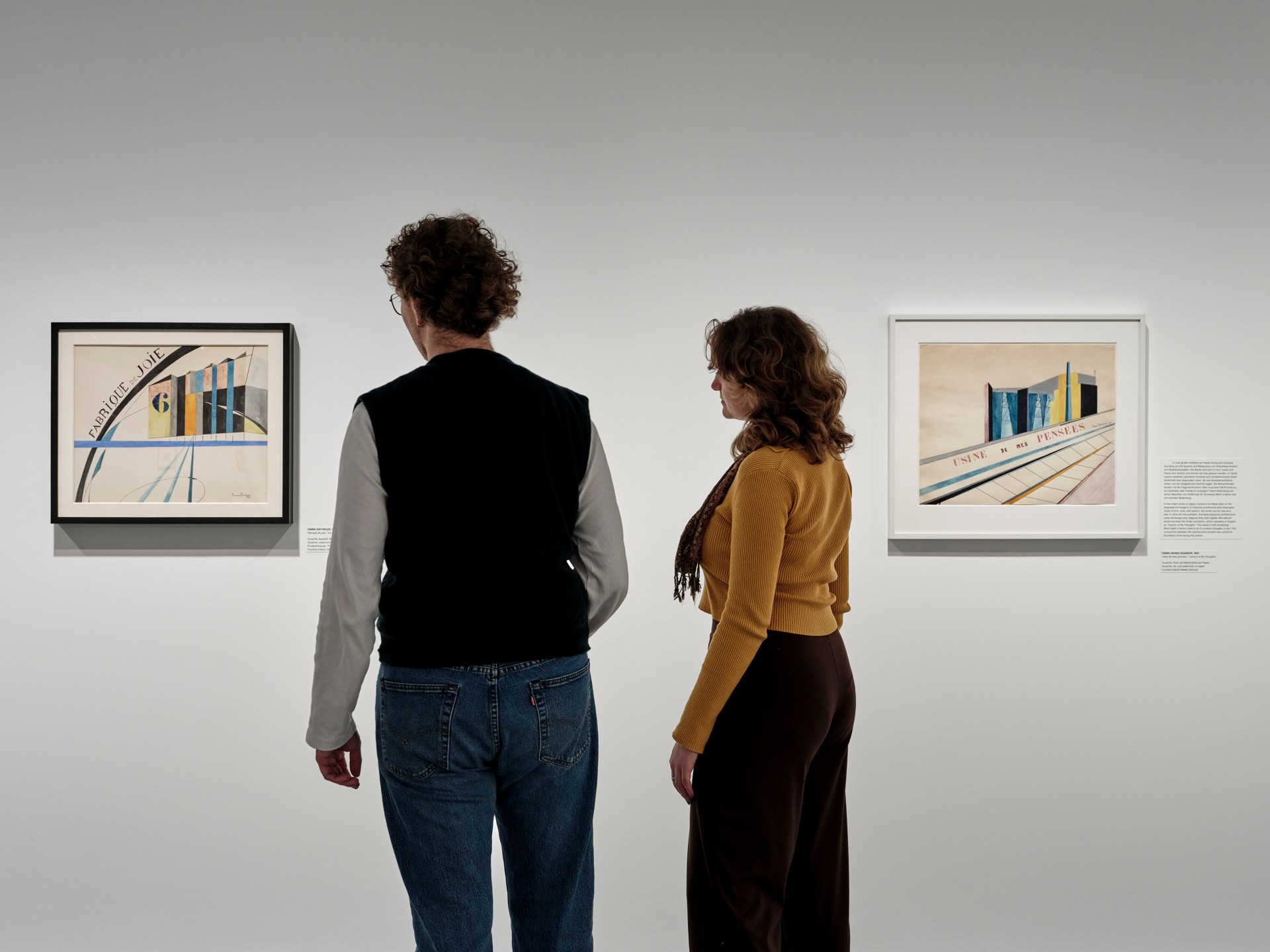 Zwei Personen betrachten in einer Galerie moderne Kunstwerke vor neutralen Wänden.