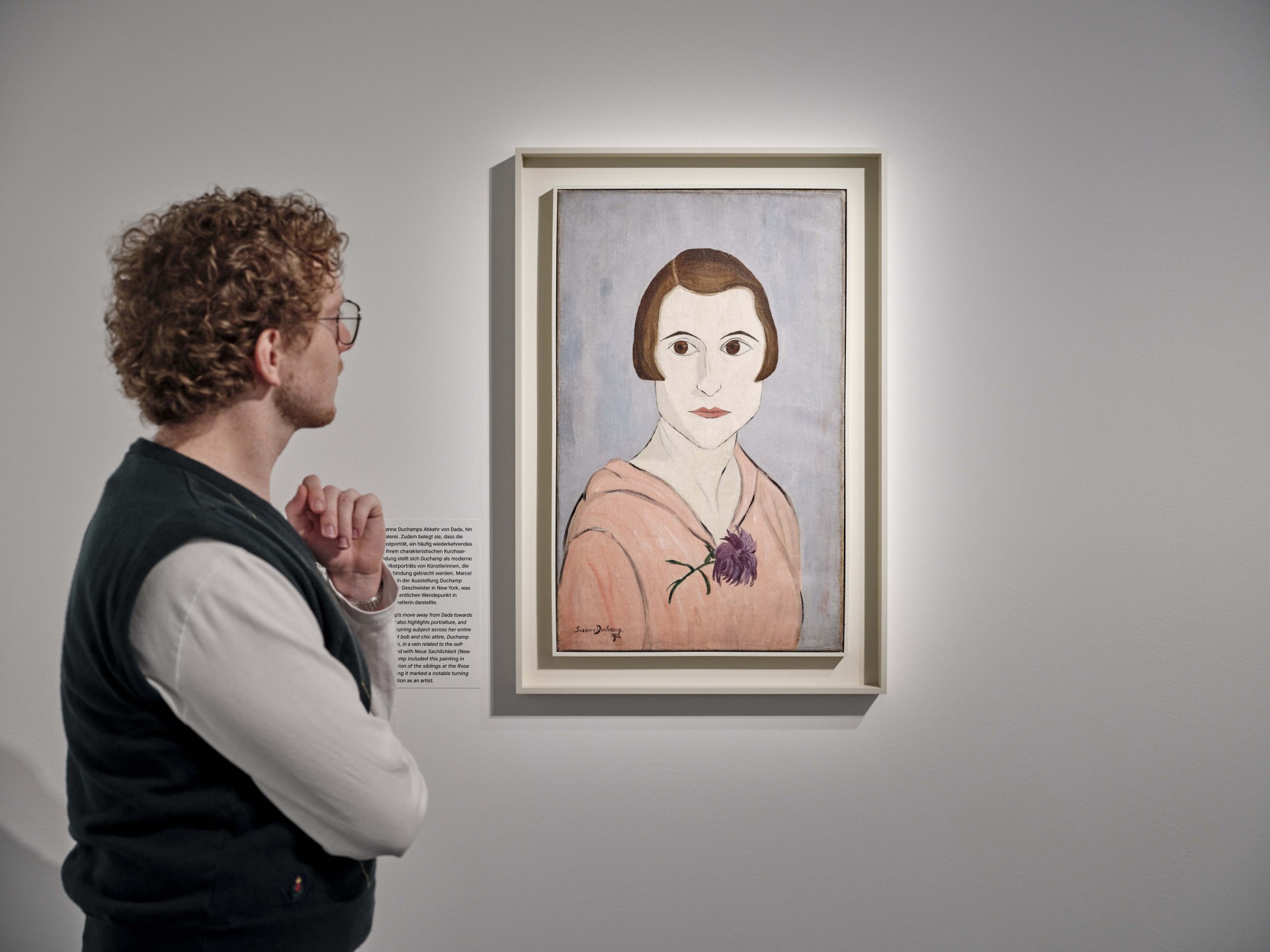 Ein Besucher betrachtet das Porträt einer Frau mit einer Blume in einem modernen Kunstmuseum.