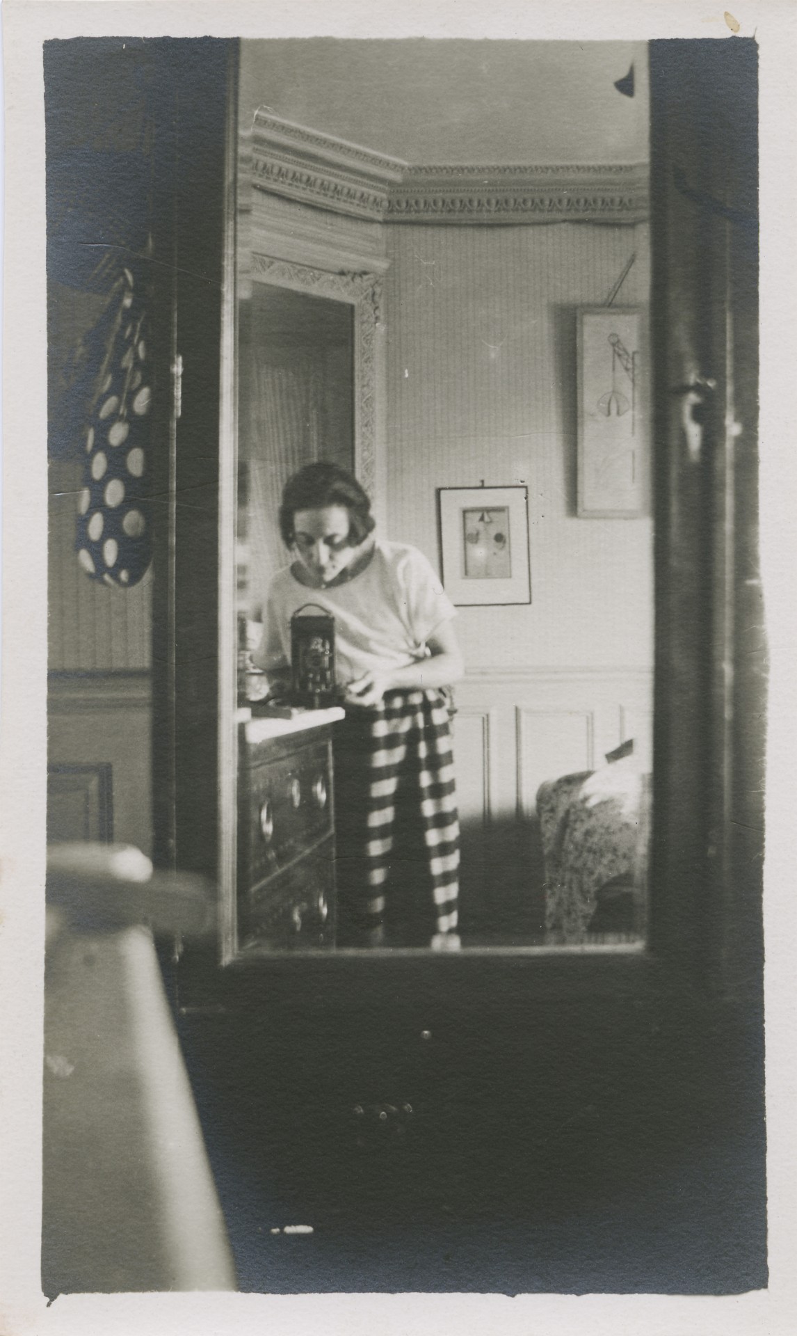 Eine Frau in gestreifter Kleidung steht vor einem Möbelstück und betrachtet etwas in einem dekorierten Raum.