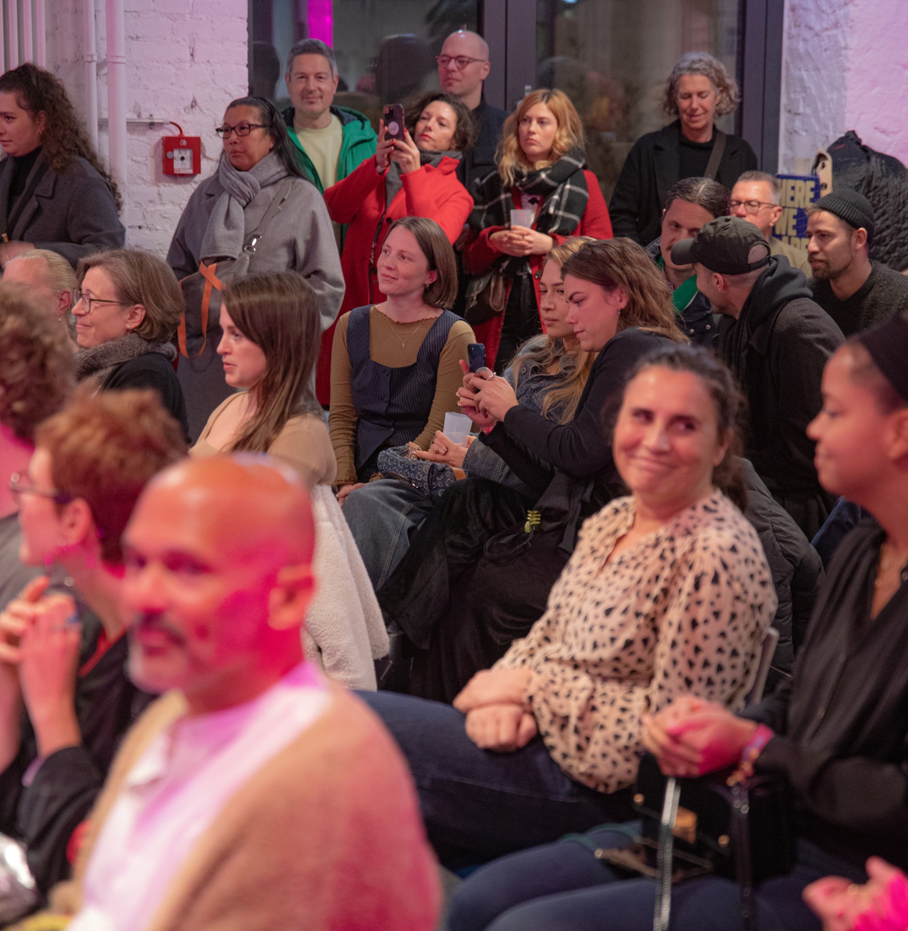 Eine Gruppe von Menschen sitzt und steht in einem modernen Veranstaltungsraum, viele nutzen ihre Handys.